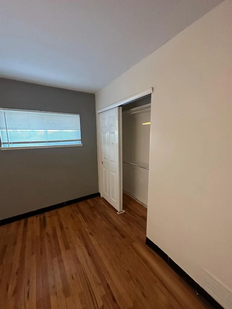 Empty room with wood flooring, a window with blinds, and a closet with a sliding door.