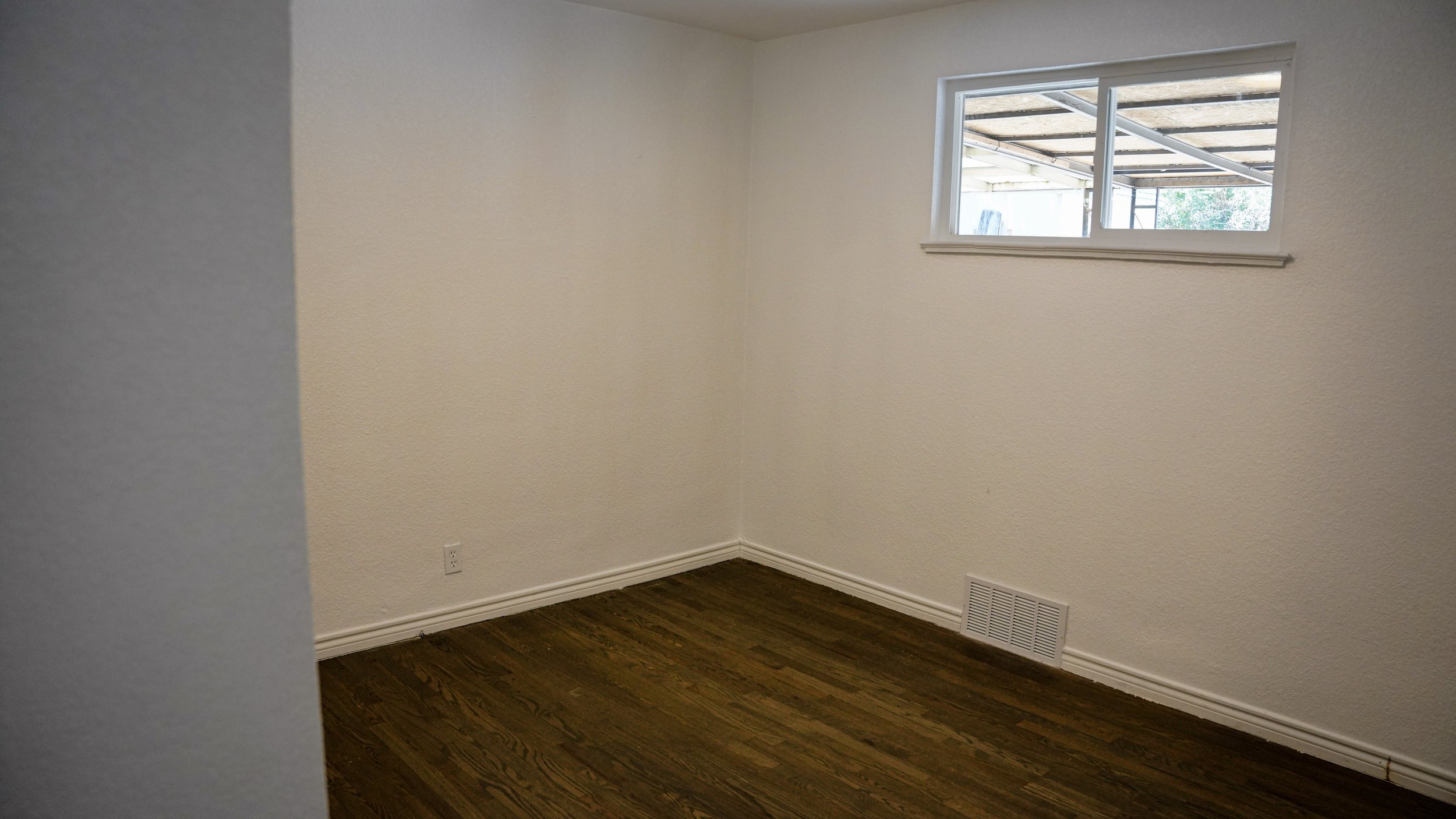 Empty room with white walls, a small window, and hardwood flooring.