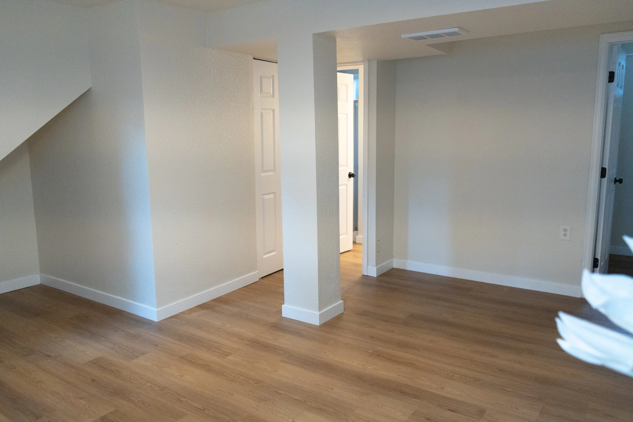 Empty room with light-colored walls, wooden floors, and white baseboards, with open doors to other rooms.