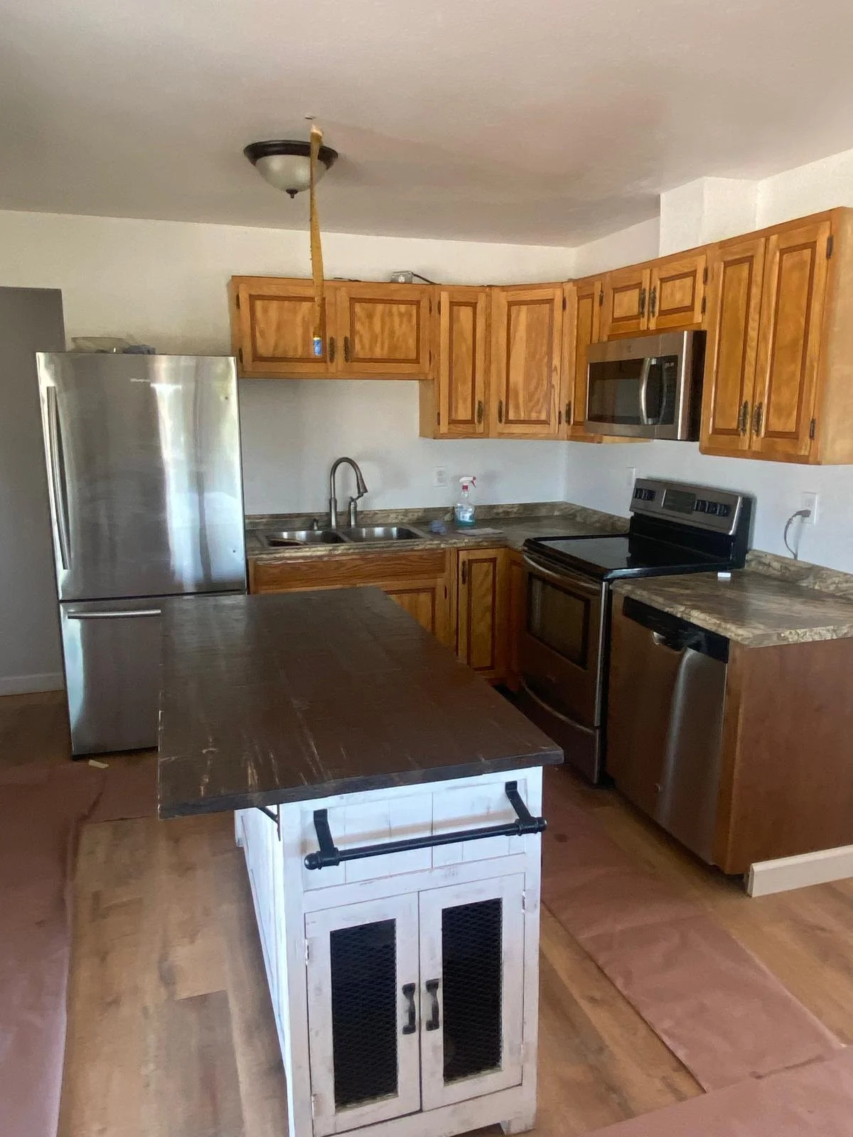 Kitchen with wooden cabinets, stainless steel fridge, microwave, oven, dishwasher, double sink, and island with wood top and white base cabinets.
