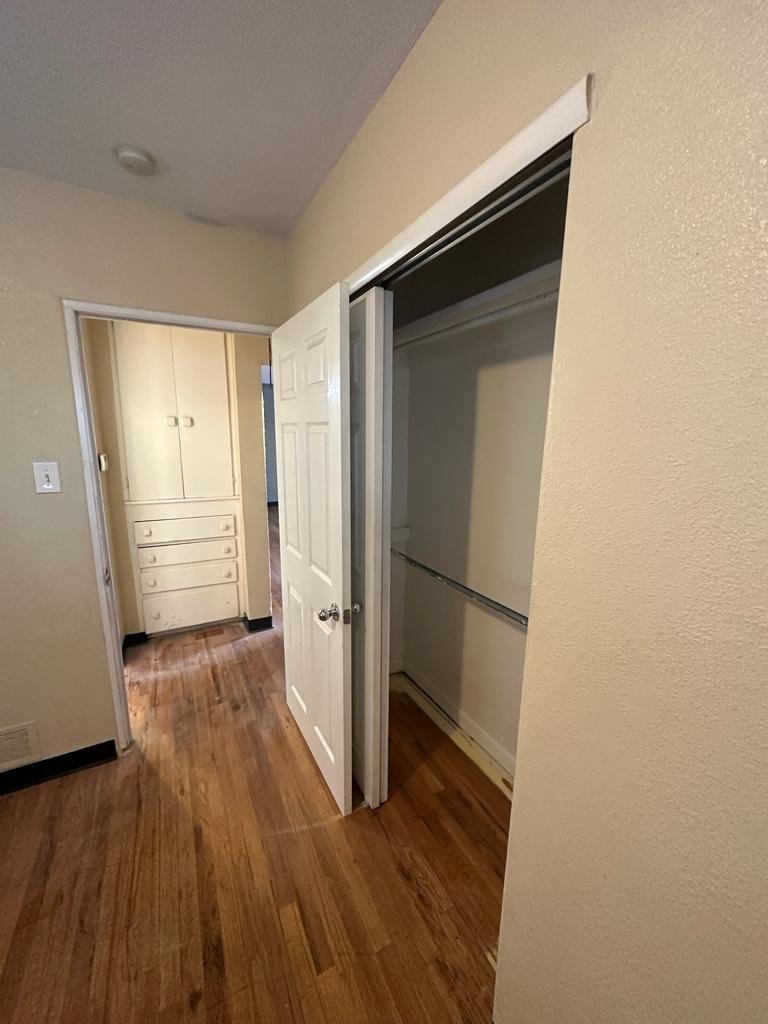 Empty closet with sliding door in a room with wooden floor and beige walls.