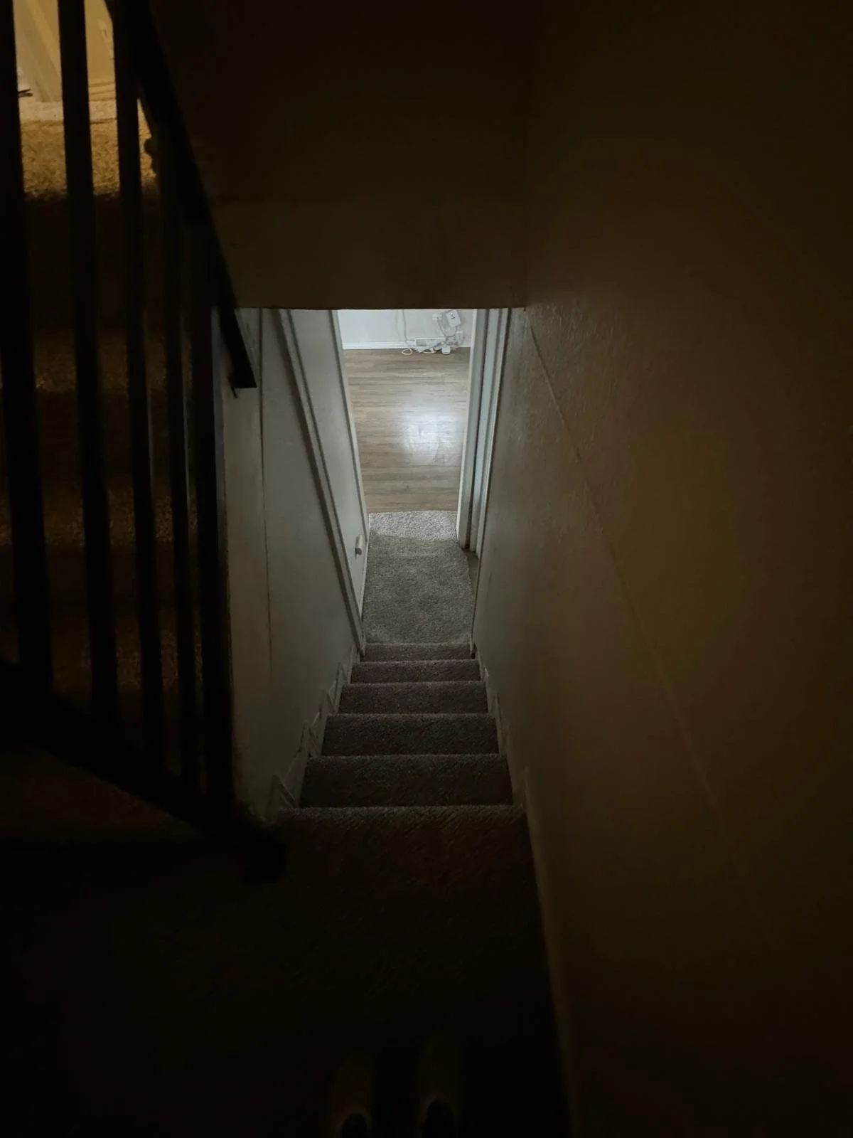 Indoor view of a staircase leading down to a hallway with a door open into a room with wooden flooring.