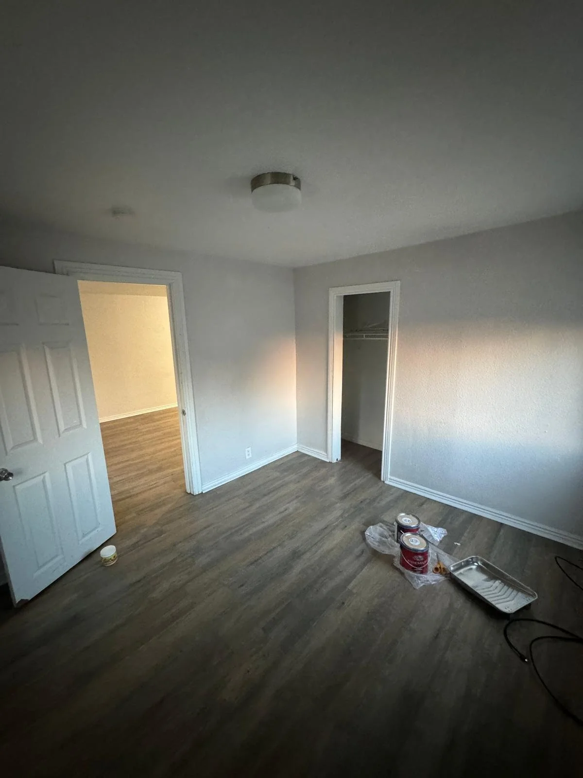 Empty room with painted white walls, dark wood flooring, an open closet, and some painting supplies on the floor.