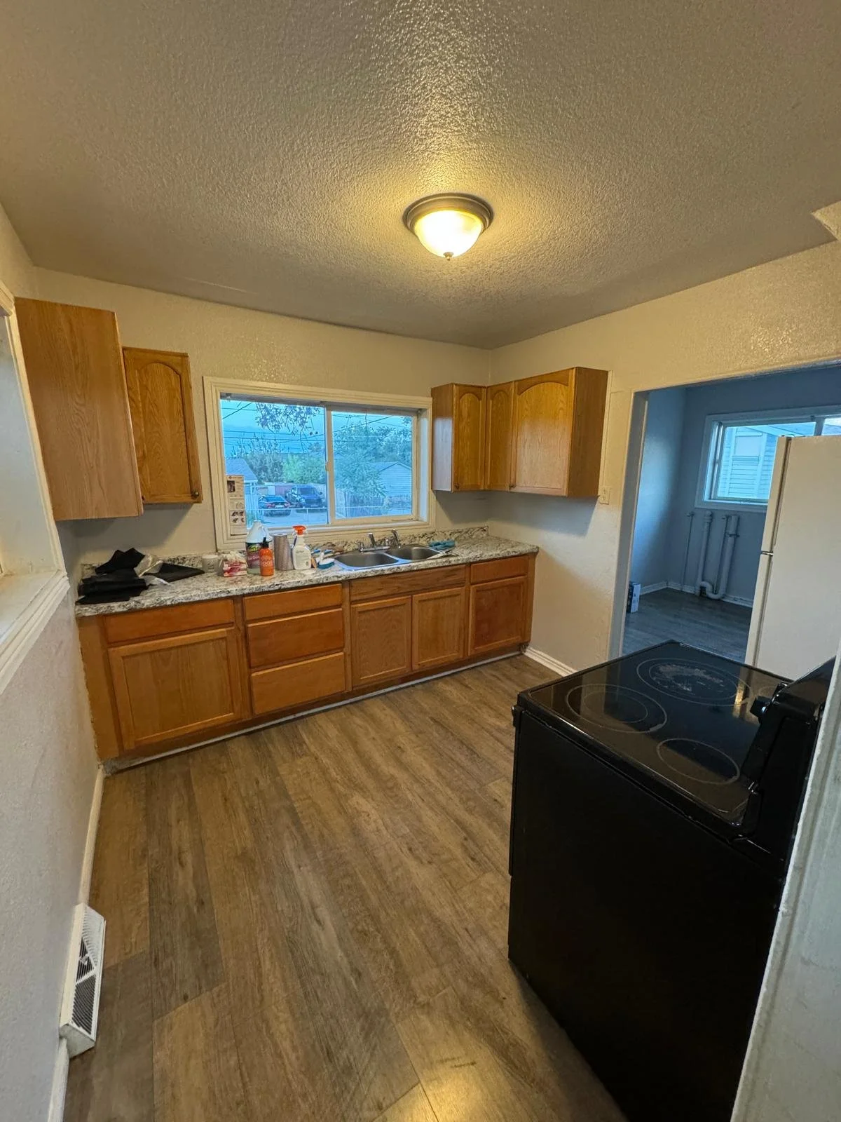 A small kitchen with wooden cabinets, a granite countertop, a window above the sink, and a black stove.