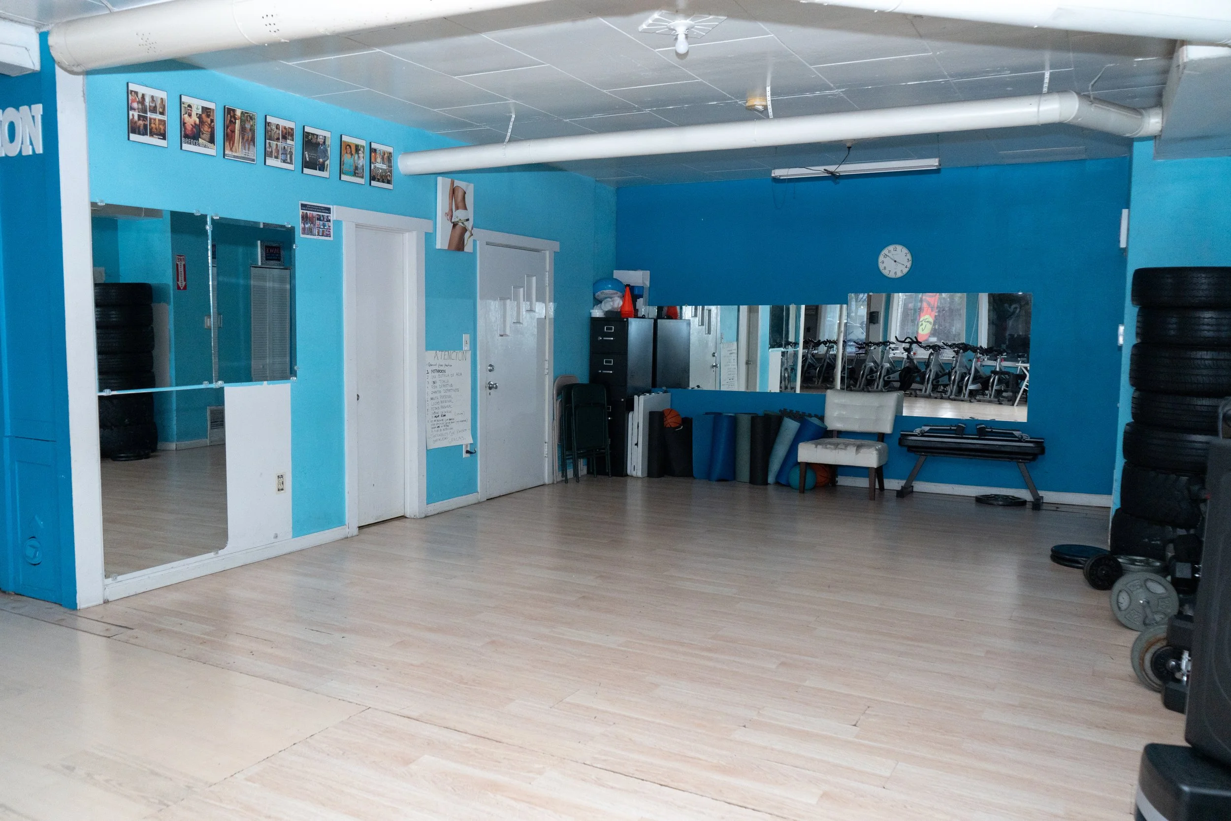 An empty exercise room with blue walls, mirrors, and various gym equipment like weights, mats, and workout machines.