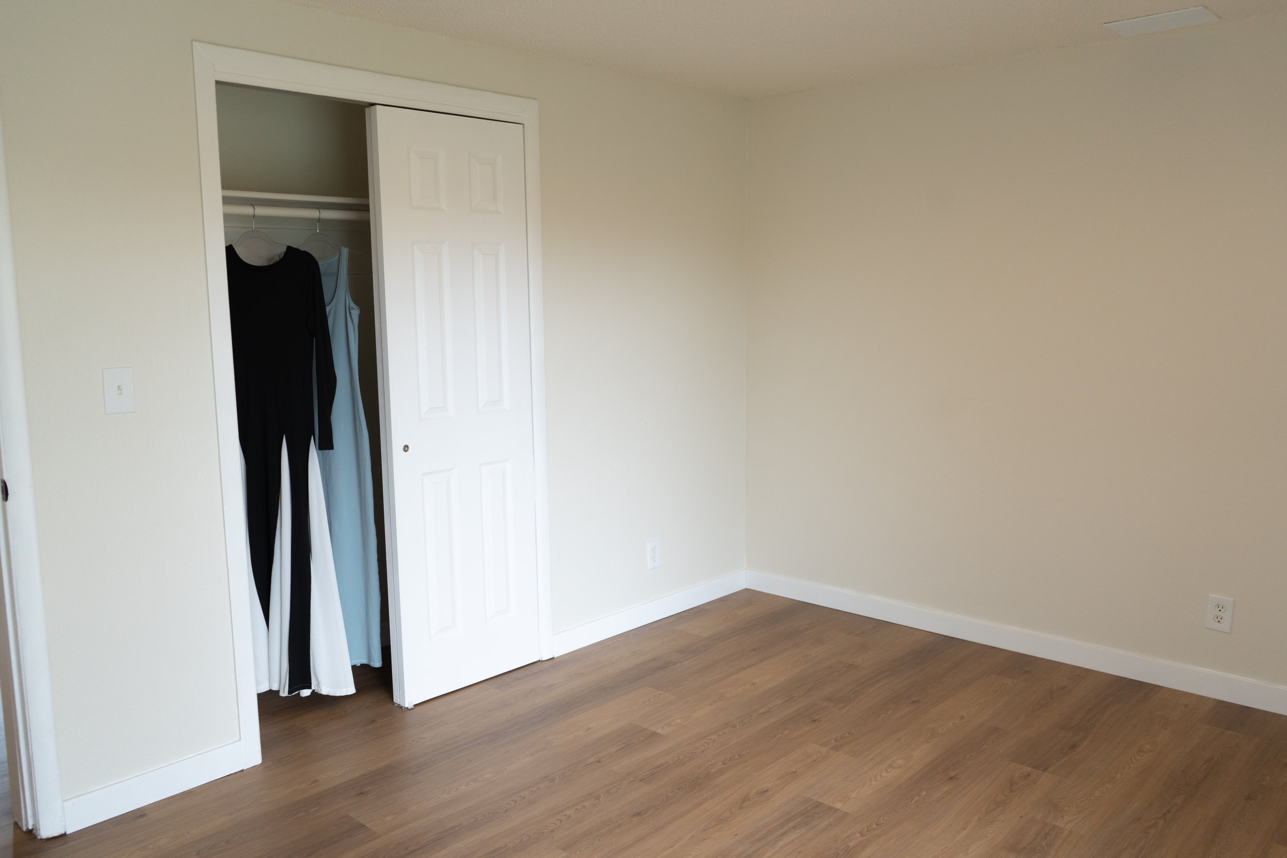 Empty room with a closet containing clothes and a wooden floor.