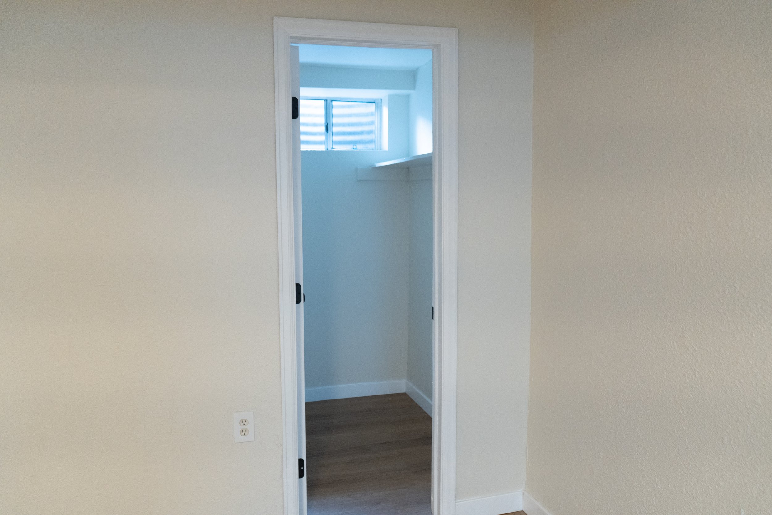 An interior view of an empty room with beige walls and a doorway leading to a small room with a window, white walls, and wooden flooring.