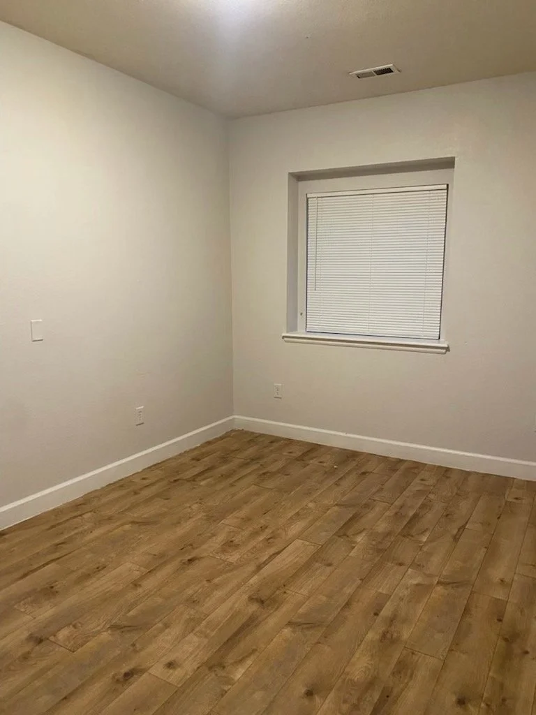 Empty room with white walls, a window with closed blinds, and wooden flooring.