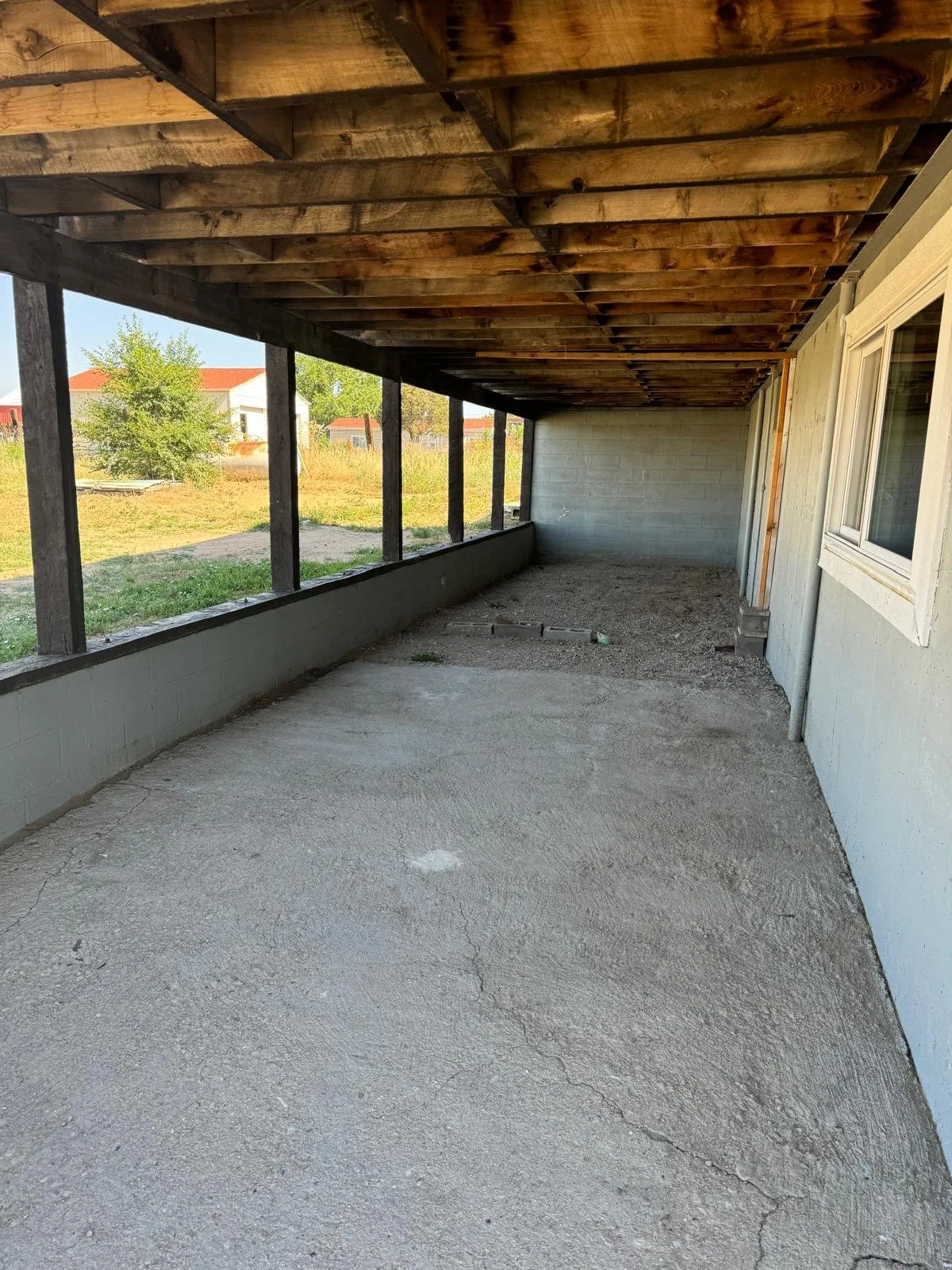 Enclosed porch with concrete floor, wooden ceiling, and cinder block wall, with a view of yard and neighboring houses.