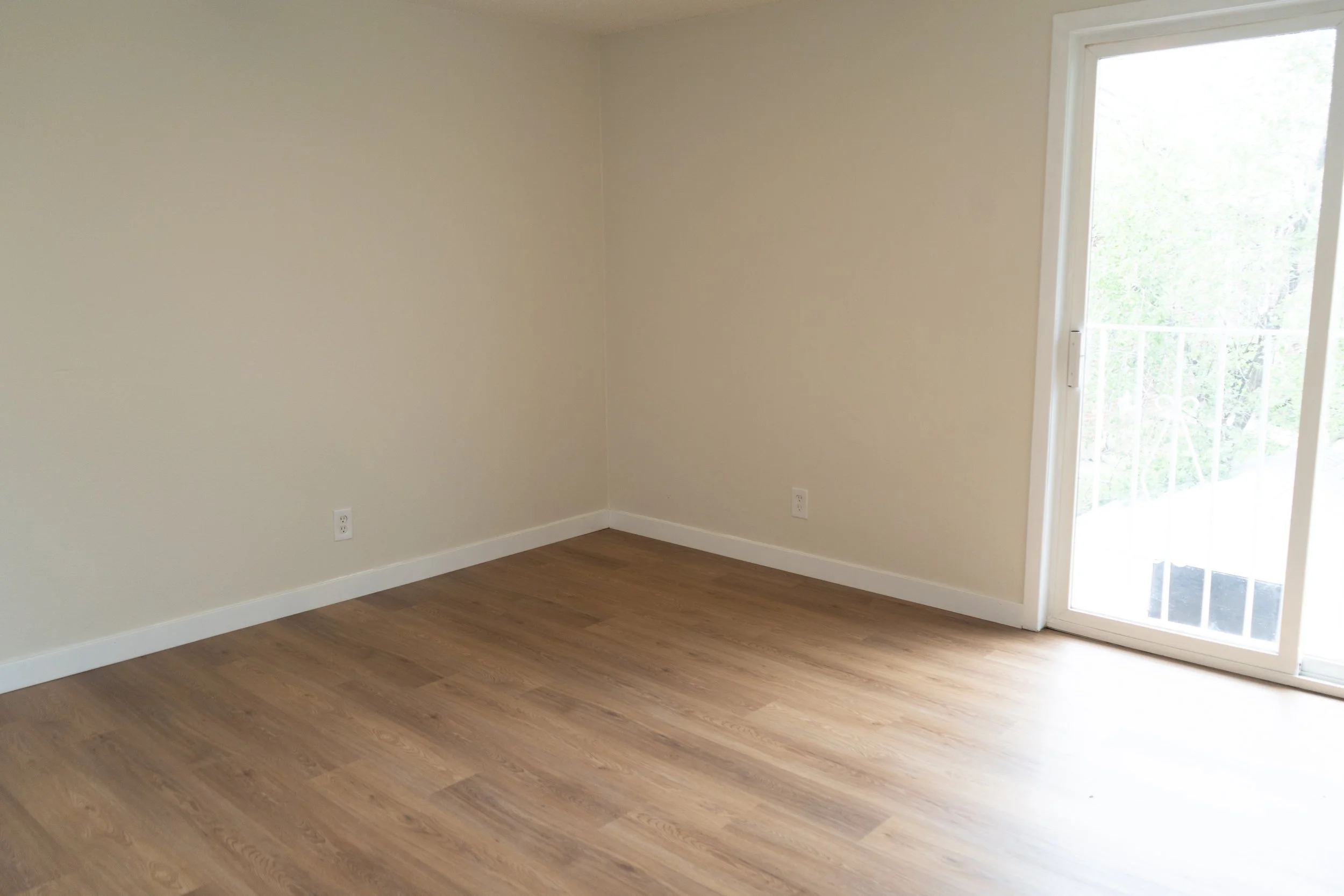 Empty room with beige walls, wooden flooring, and a sliding glass door leading to a balcony.