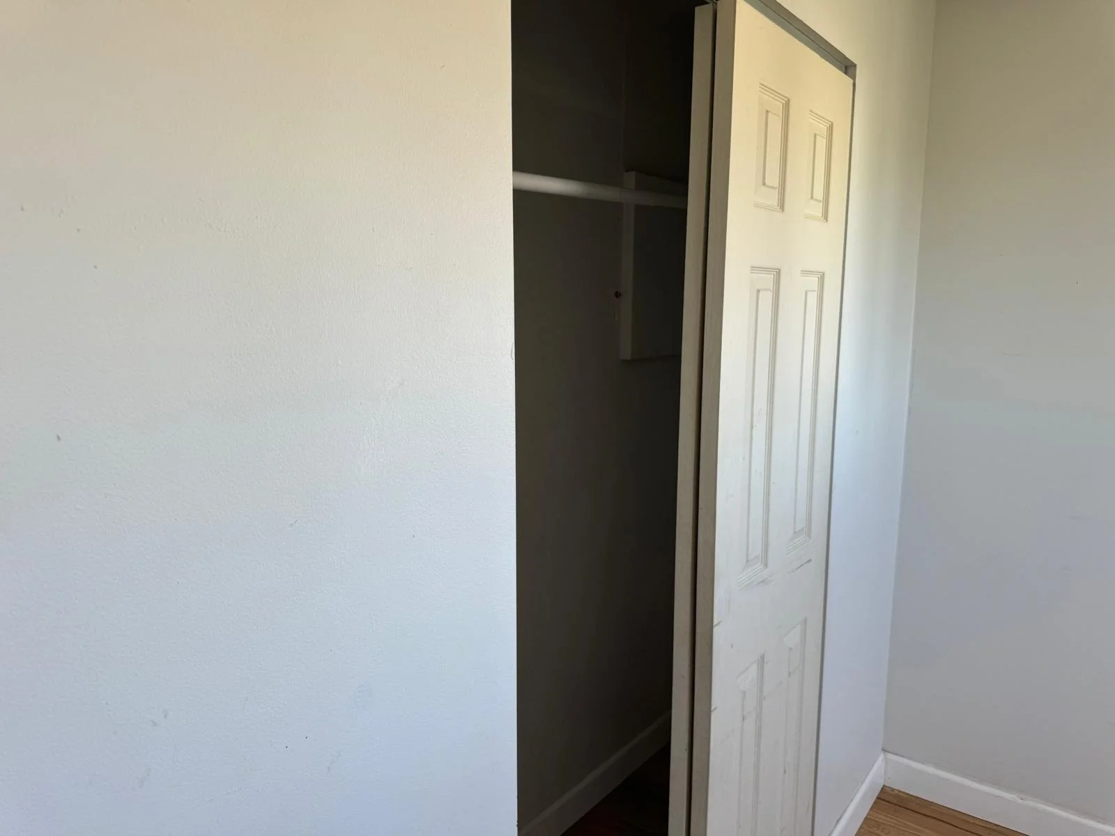 Empty closet with white door slightly ajar in a room with white walls and a hardwood floor.