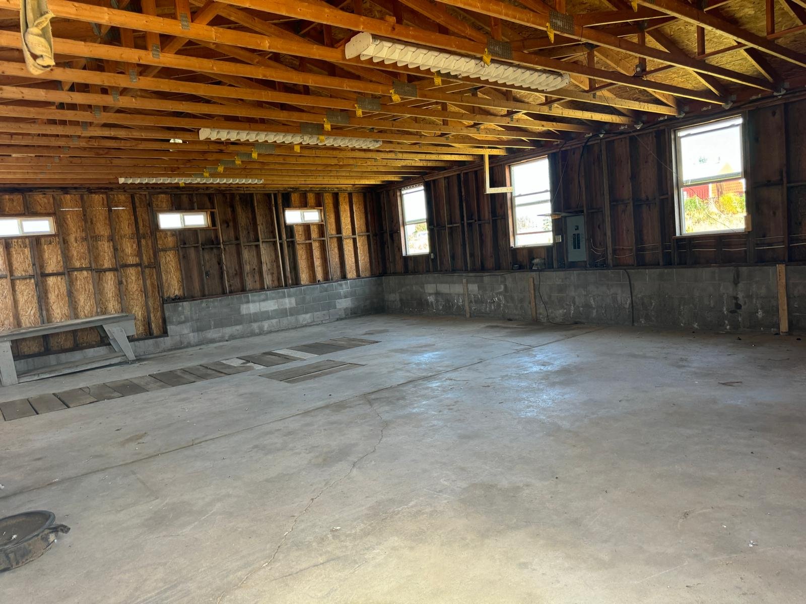 Empty garage with concrete floor, unfinished walls, and exposed wooden beams on the ceiling, with several small windows on the side walls.