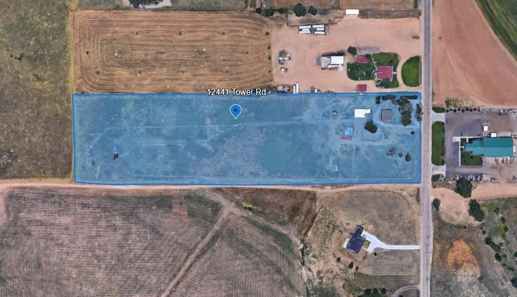 A satellite view of a rectangular plot of land outlined in blue, located on Tower Road, with surrounding fields, roads, and residential properties.