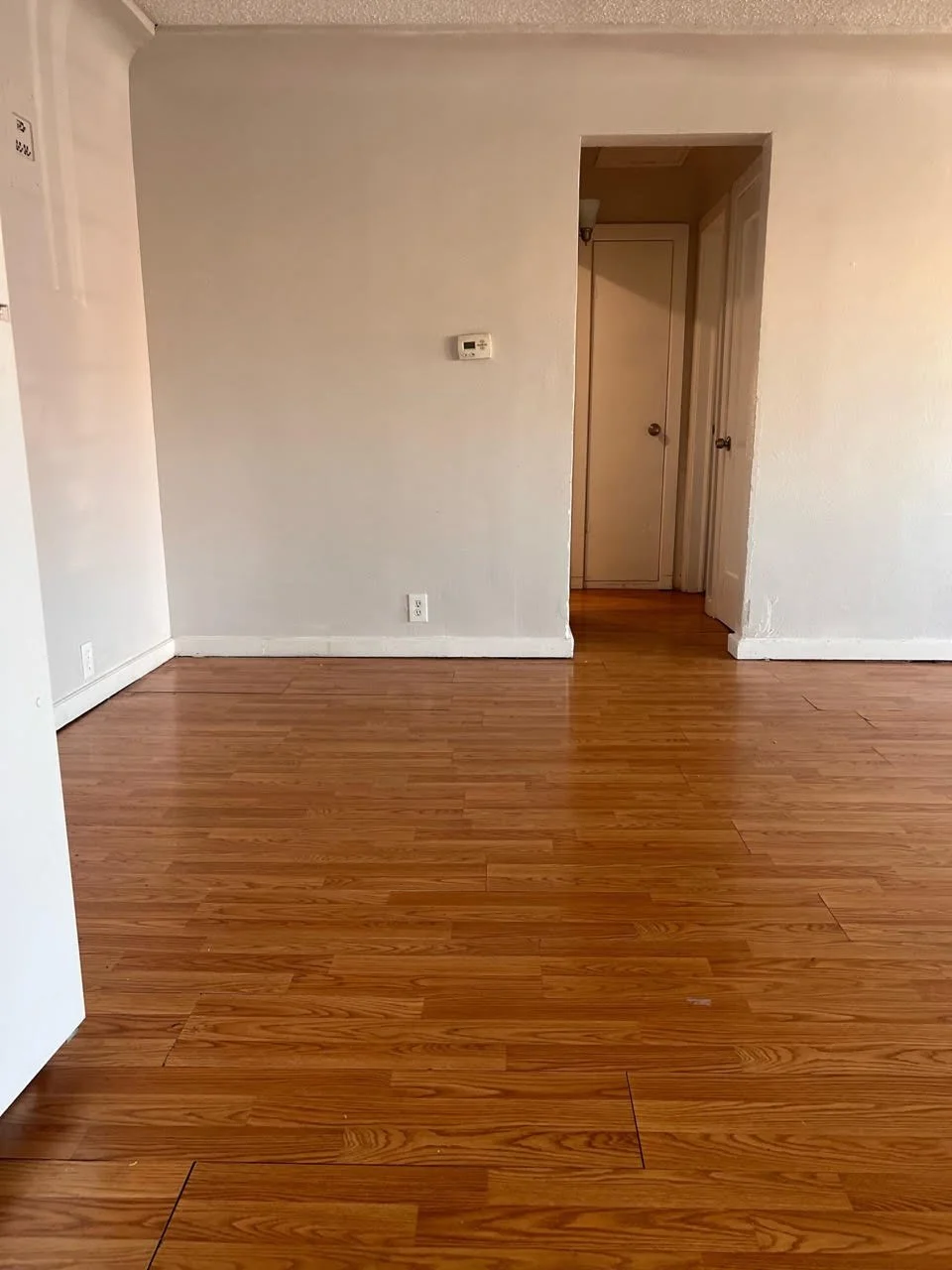 Empty room with wooden flooring, white walls, and an open doorway leading to a hallway.