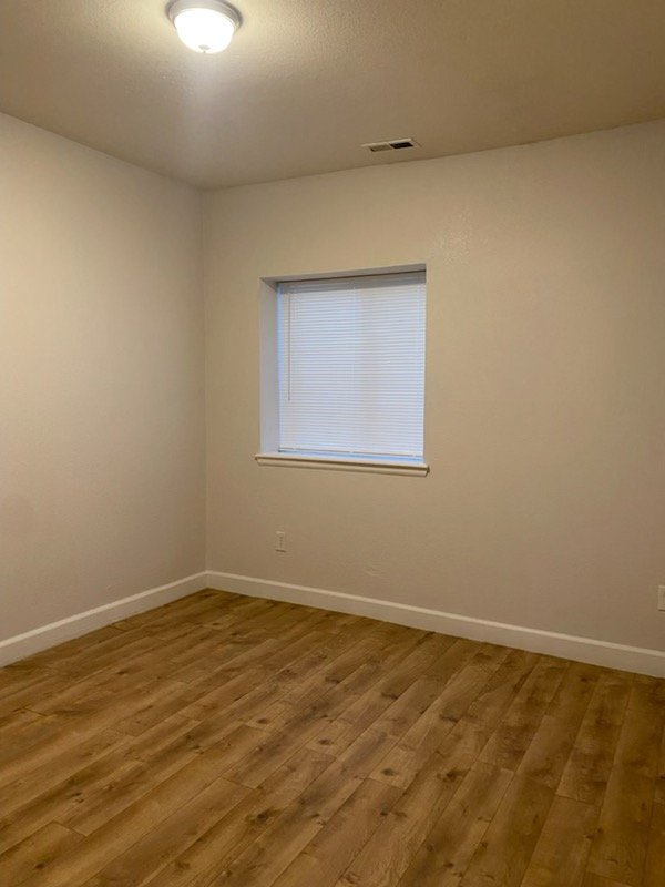 Empty room with wood flooring, plain white walls, a window with blinds, and a ceiling light.