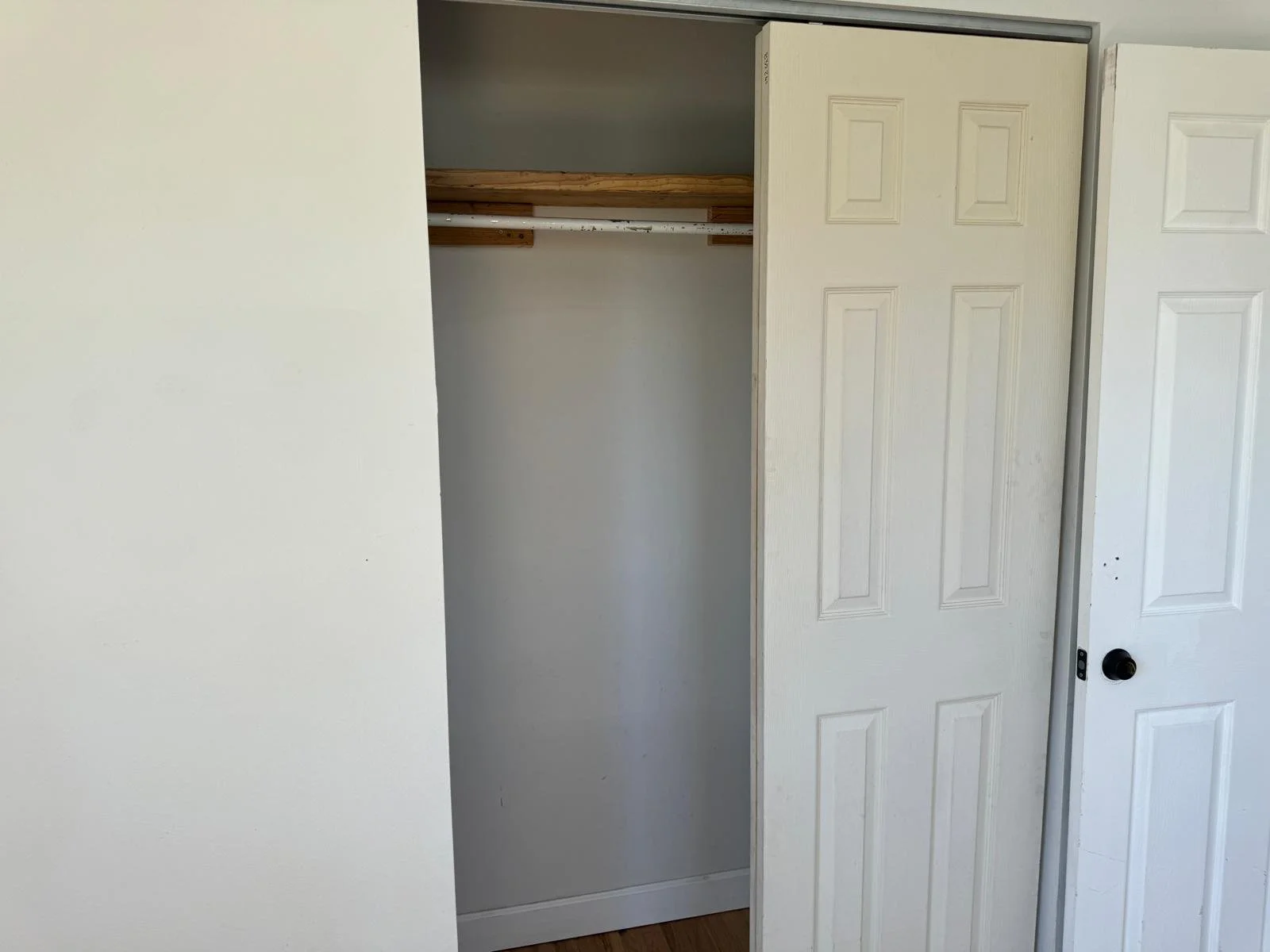 Empty closet with a partially open sliding door, white walls, and a wooden rod for hanging clothes.