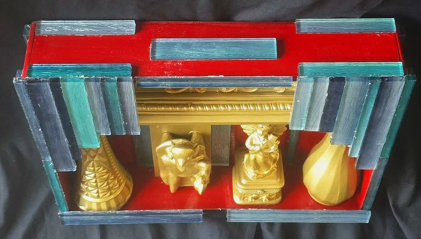 Top view of a handmade, hand-painted assemblage box containing painted and glued found objects.