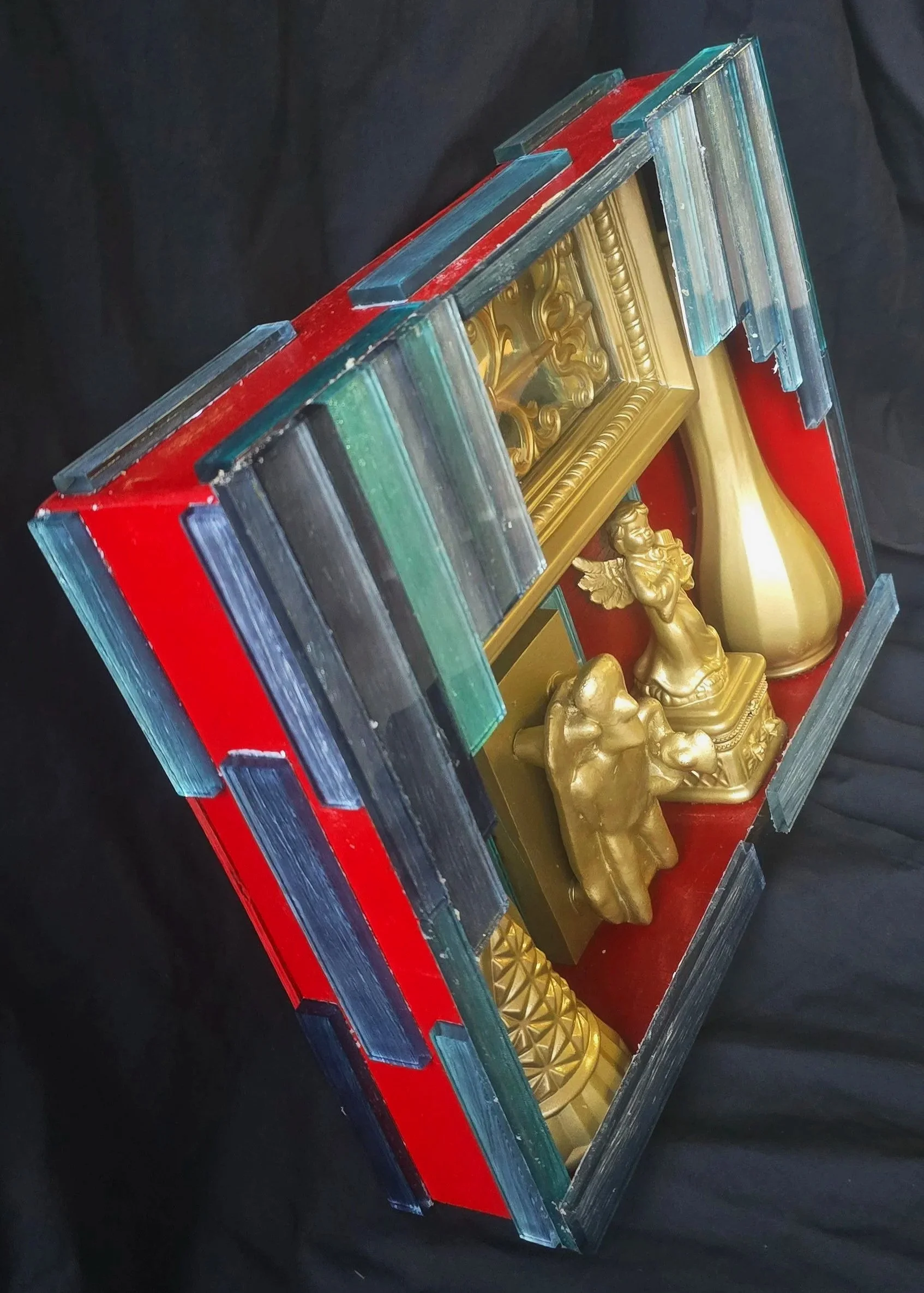 Left view of a handmade, hand-painted assemblage box containing painted and glued found objects.