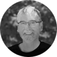 Black and white photo of a smiling man with glasses and short hair, outdoors with blurred trees in the background.