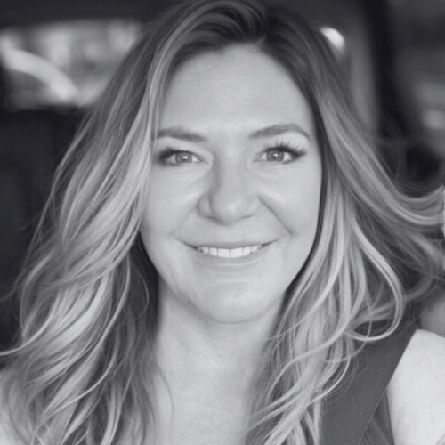 Black and white photo of a woman with wavy, shoulder-length hair smiling at the camera, inside a vehicle.