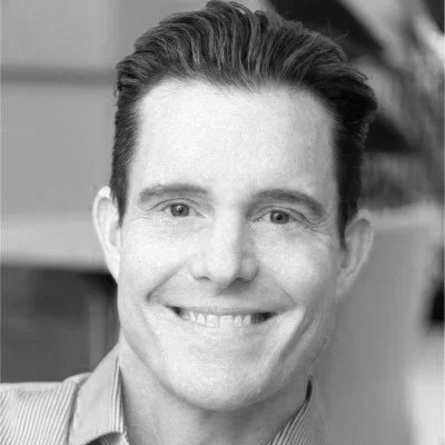 Black and white photo of a smiling man with short, dark hair, wearing a collared shirt.