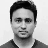 A black and white portrait of a man with short dark hair, wearing a dark shirt, facing the camera with a slight smile.