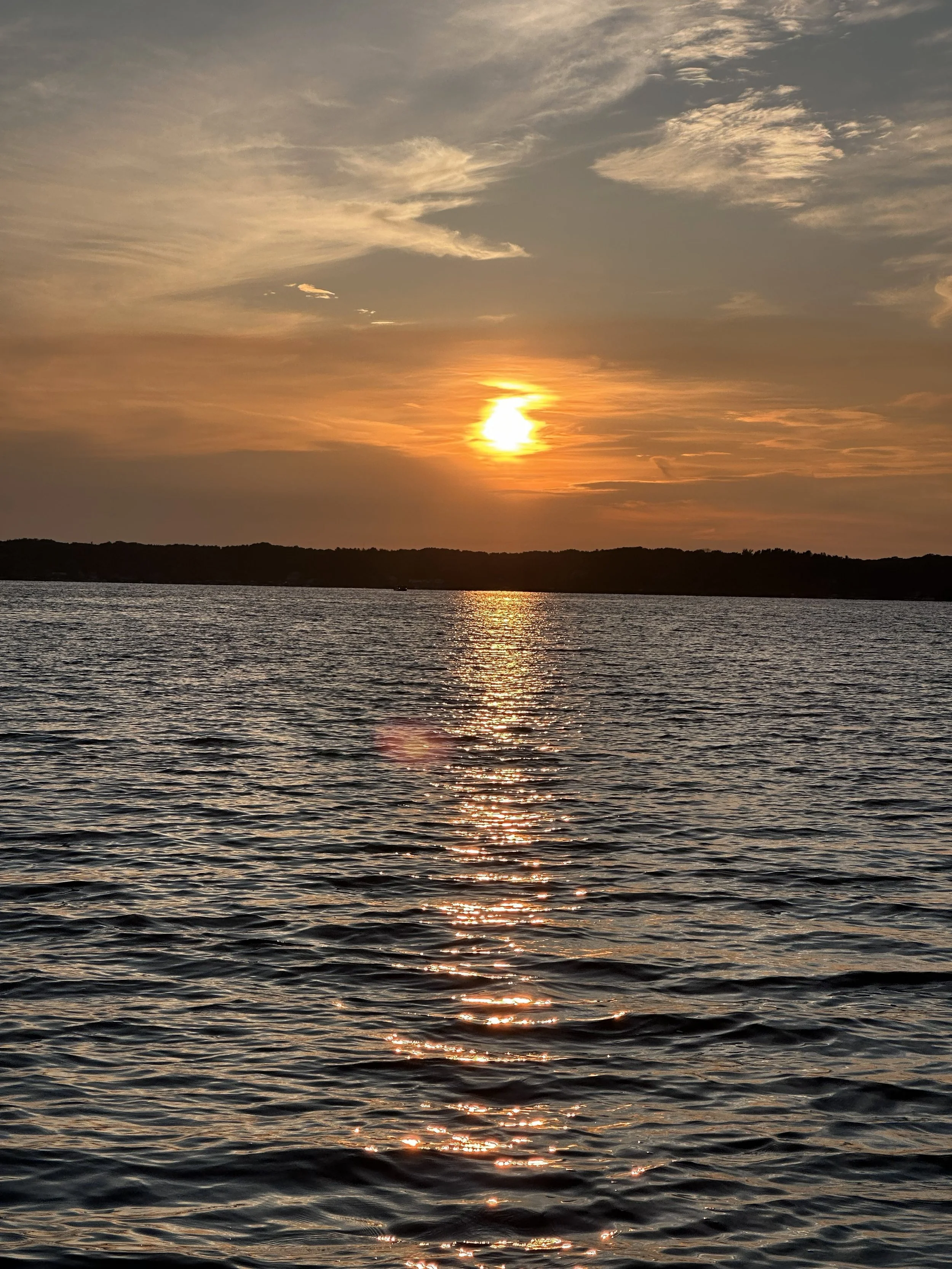 Sunset over a calm body of water with a reflection of the sky and clouds on the surface.