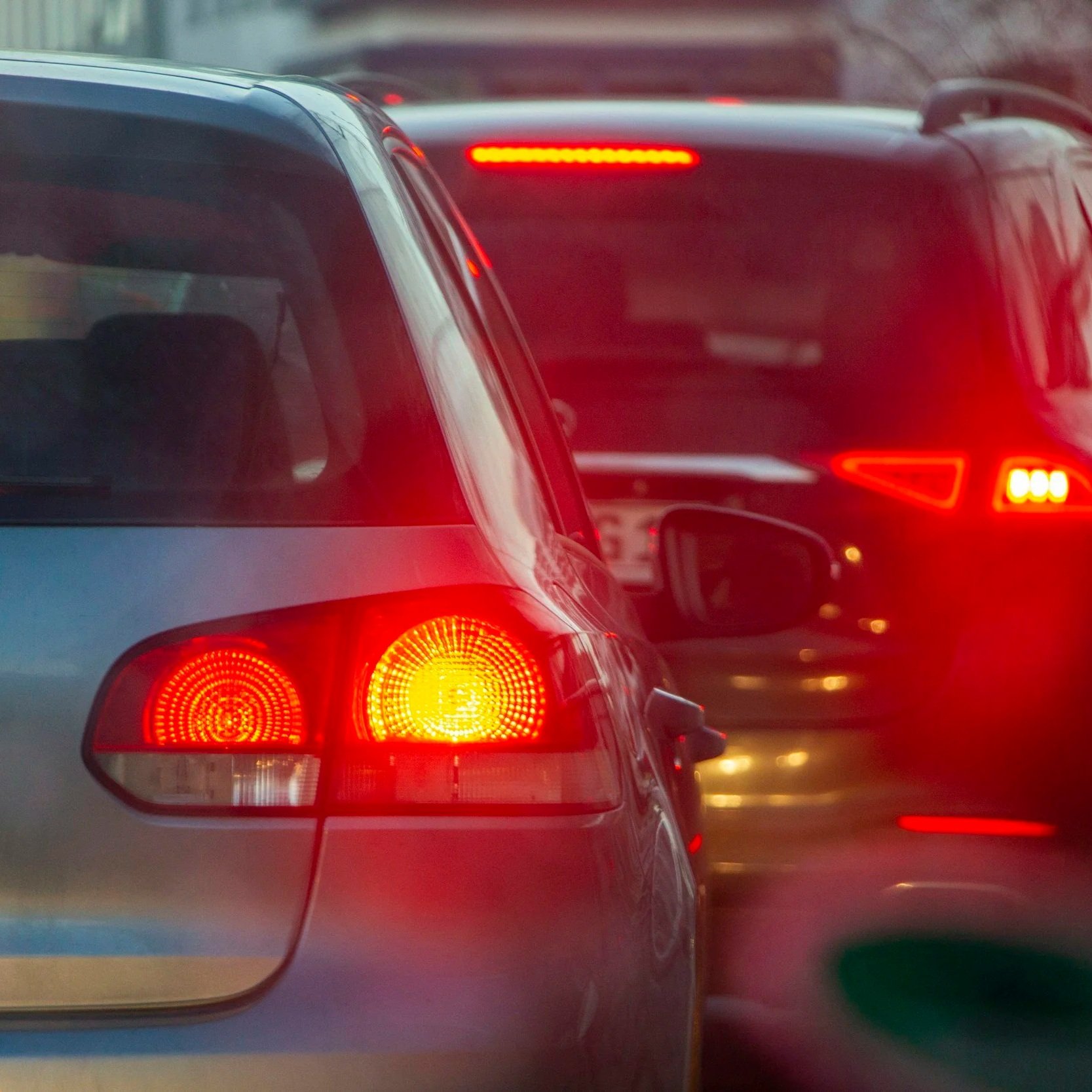 Traffic jam with cars on the road, rear lights illuminated, cloudy weather.