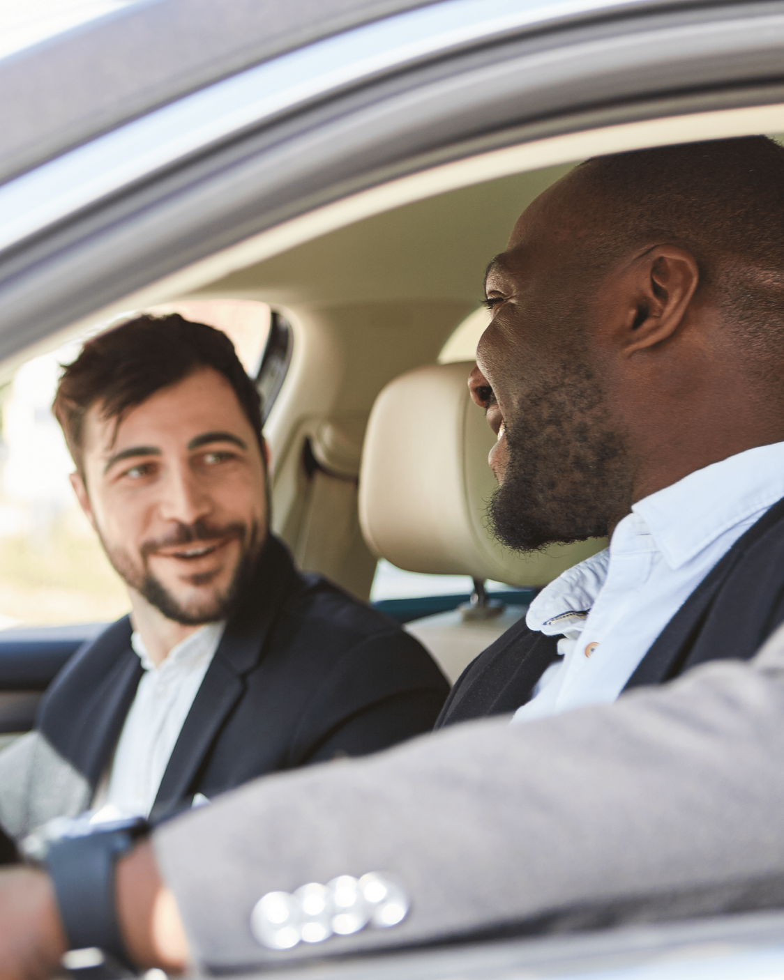 Two men sitting in a car, engaged in conversation, smiling.