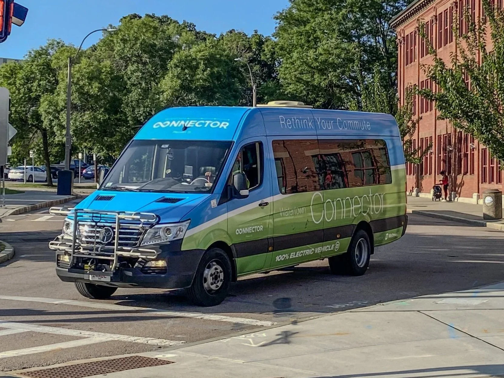 A blue and green electric shuttle bus with the words "Waterloo Connector" on the side and the slogan "Rethink Your Commute" on the top, driving on a city street.