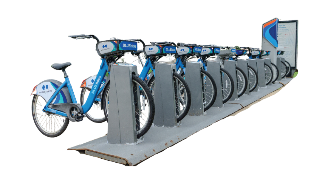 A row of blue rental bicycles parked in a bike-sharing station with an information kiosk on the right.
