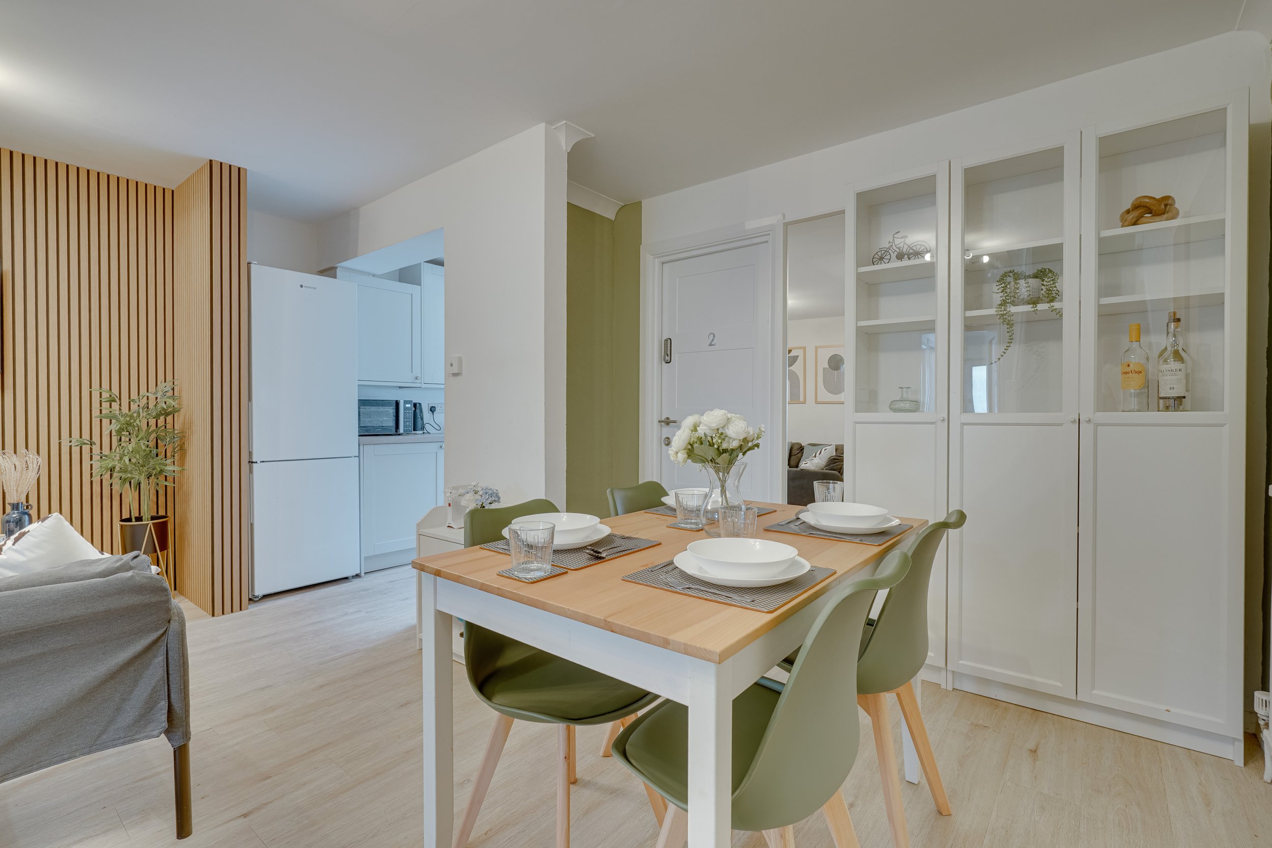Residential dining area featuring a simple wooden table with green dining chairs, open-plan connection to the kitchen and living space, and soft natural tones creating a cohesive, welcoming interior.