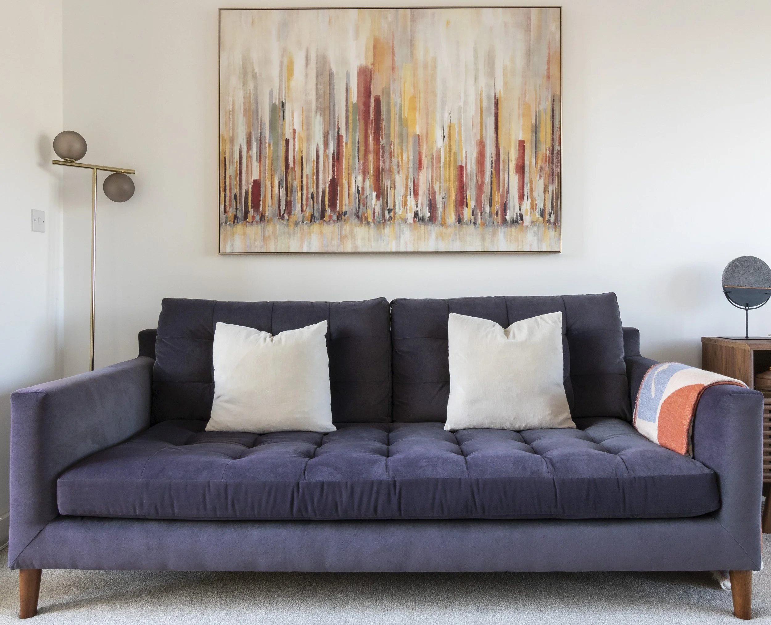 Residential living room interior featuring a deep-toned upholstered sofa, neutral cushions, statement artwork, and balanced lighting creating a refined, comfortable space.