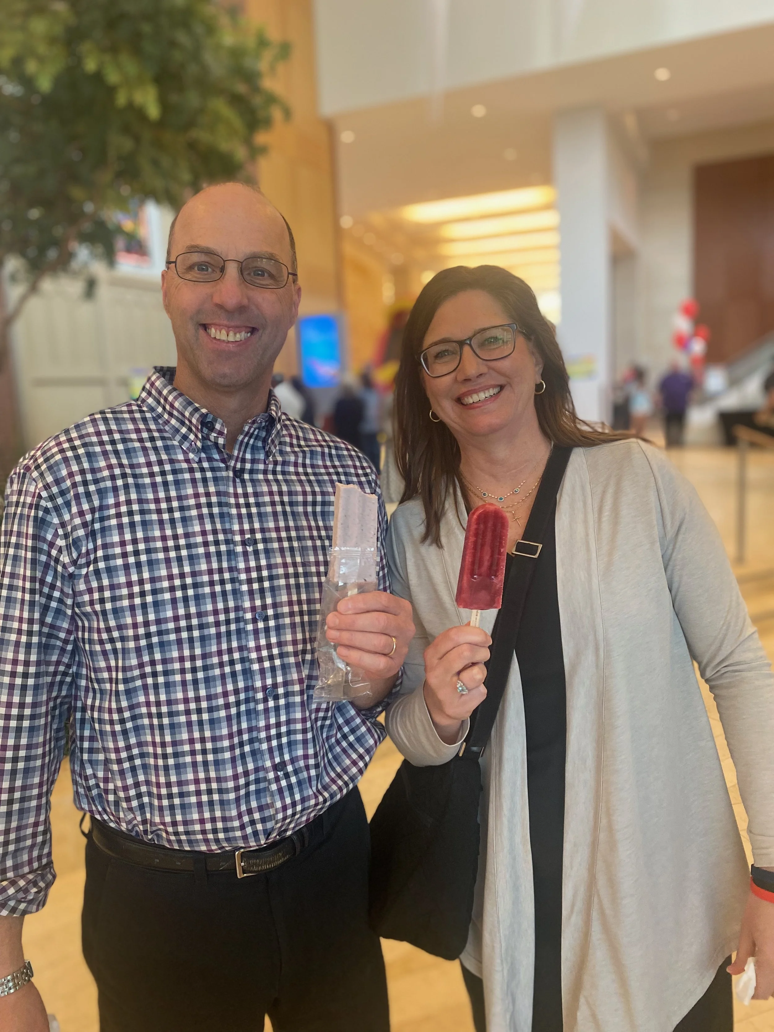 Smiling man and woman holding ice pops in a public indoor space.