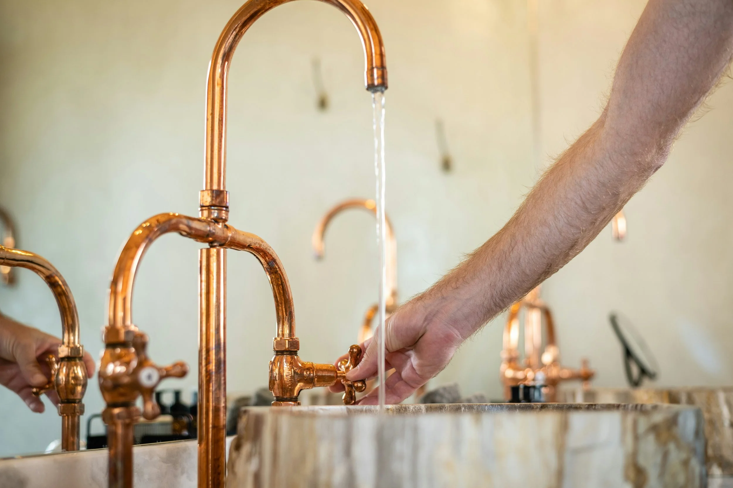Person turning on a copper faucet in a kitchen with other copper faucets in the background.