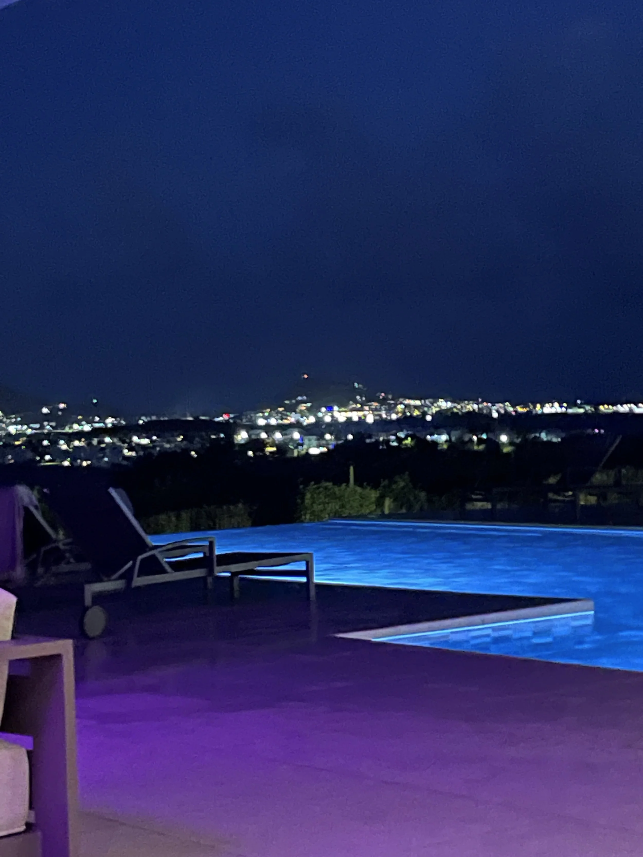 Swimming pool at night with city lights and dark sky in the background.