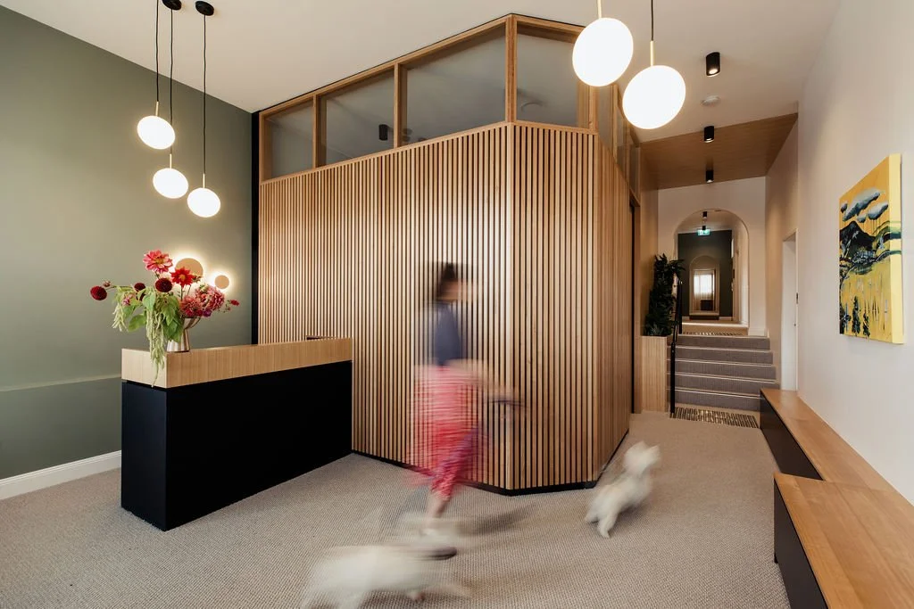 Modern interior with a green accent wall, wooden slatted partition, floating wooden bench, colorful flower arrangement, abstract painting, and hanging spherical light fixtures.