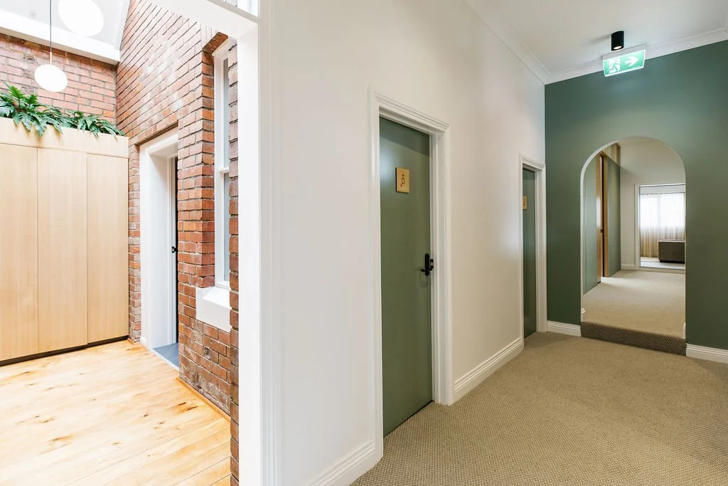 Indoor hallway with green walls, doorways, and an arched opening leading to a room with window and curtains.