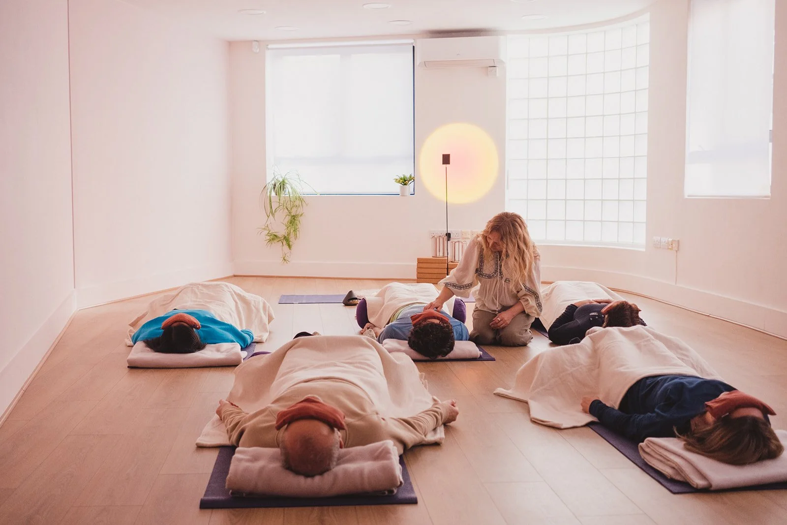 Kasia Farrar leads a group breathwork class in a bright, minimalistic room with large windows, lying on mats with her eyes closed, while others in Muswell Hill.