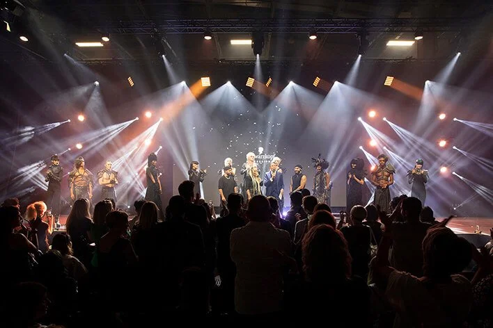 Performance artistique sur l'art de la coiffure avec des modèles sur scène.
Spectacle de coiffure mettant en avant des éclairages dramatiques et des styles variés.
Photographie professionnelle capturant l'art de la coiffure en plein spectacle.
Décors
