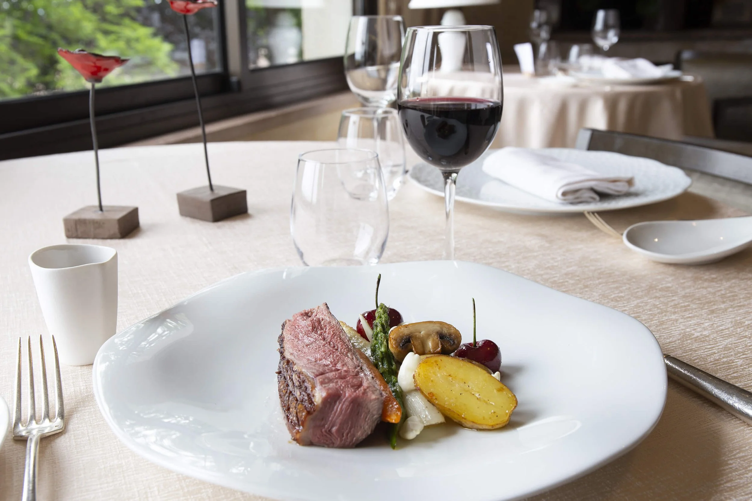 Dans un restaurant élégant, un plat gourmet préparé avec soin est accompagné de légumes frais et d’un verre de vin rouge. La photographie culinaire de François Fauré met en valeur la présentation soignée des plats. La table de dîner chic, ornée de co