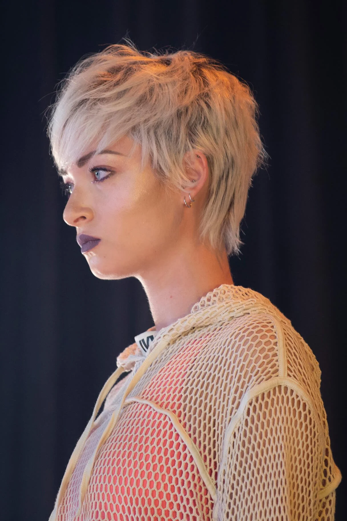 Portrait d'une coiffure moderne avec des cheveux blonds courts et un éclairage artistique.