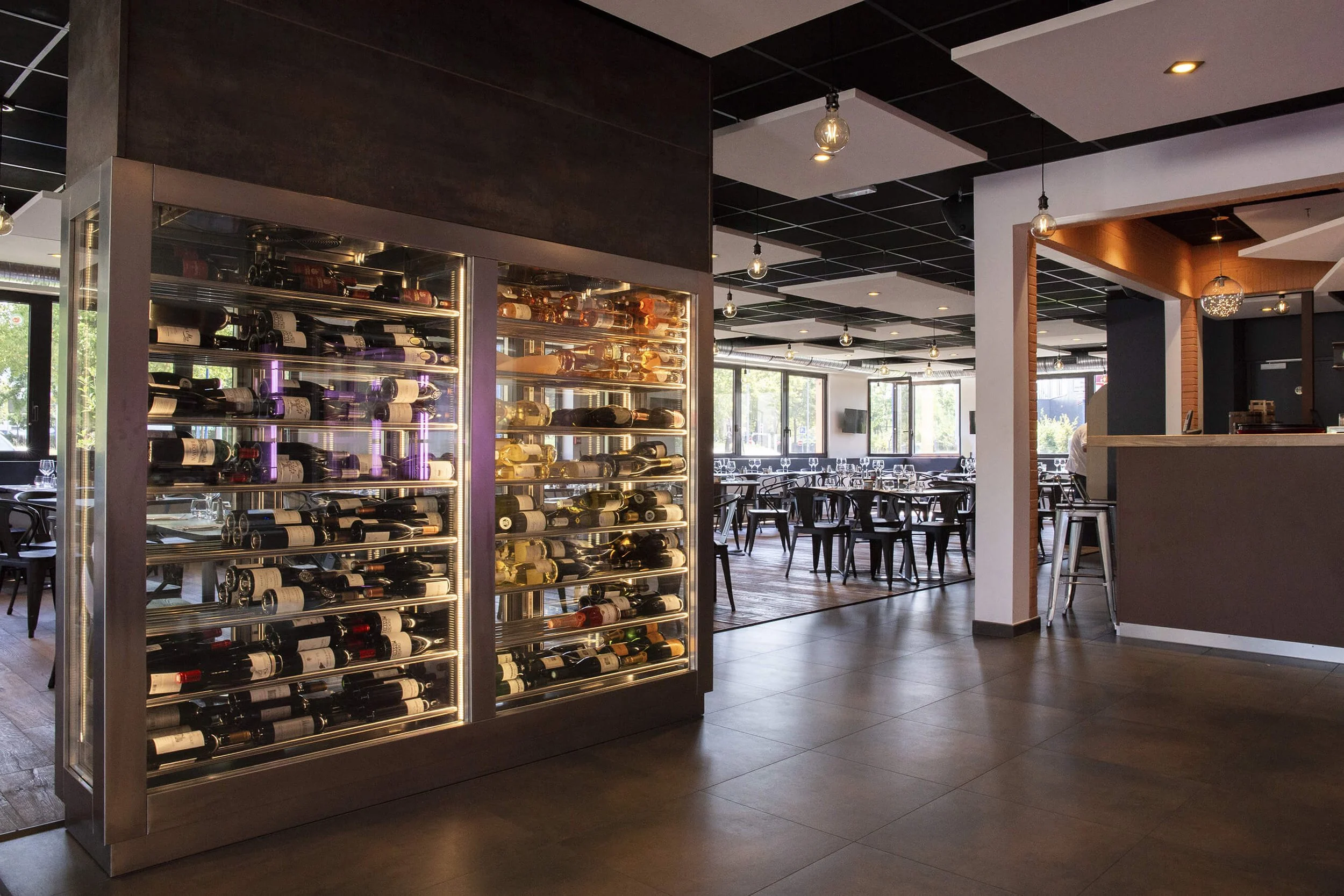 Intérieur d’un restaurant moderne avec une cave à vin élégante, capturé dans le style photographique de François Fauré.  Le décor professionnel allie éclairage moderne et mobilier chic, créant une ambiance chaleureuse. Des tables élégamment dressées 