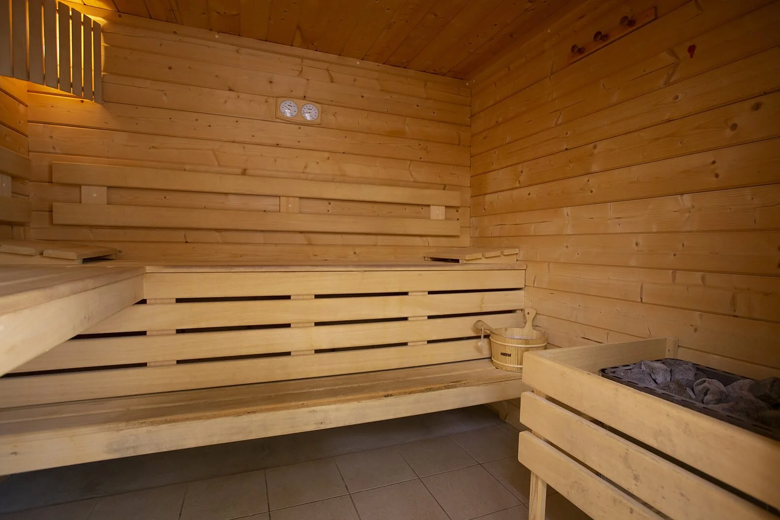 Intérieur chaleureux d’un sauna en bois, avec ses bancs en bois et son seau traditionnel.