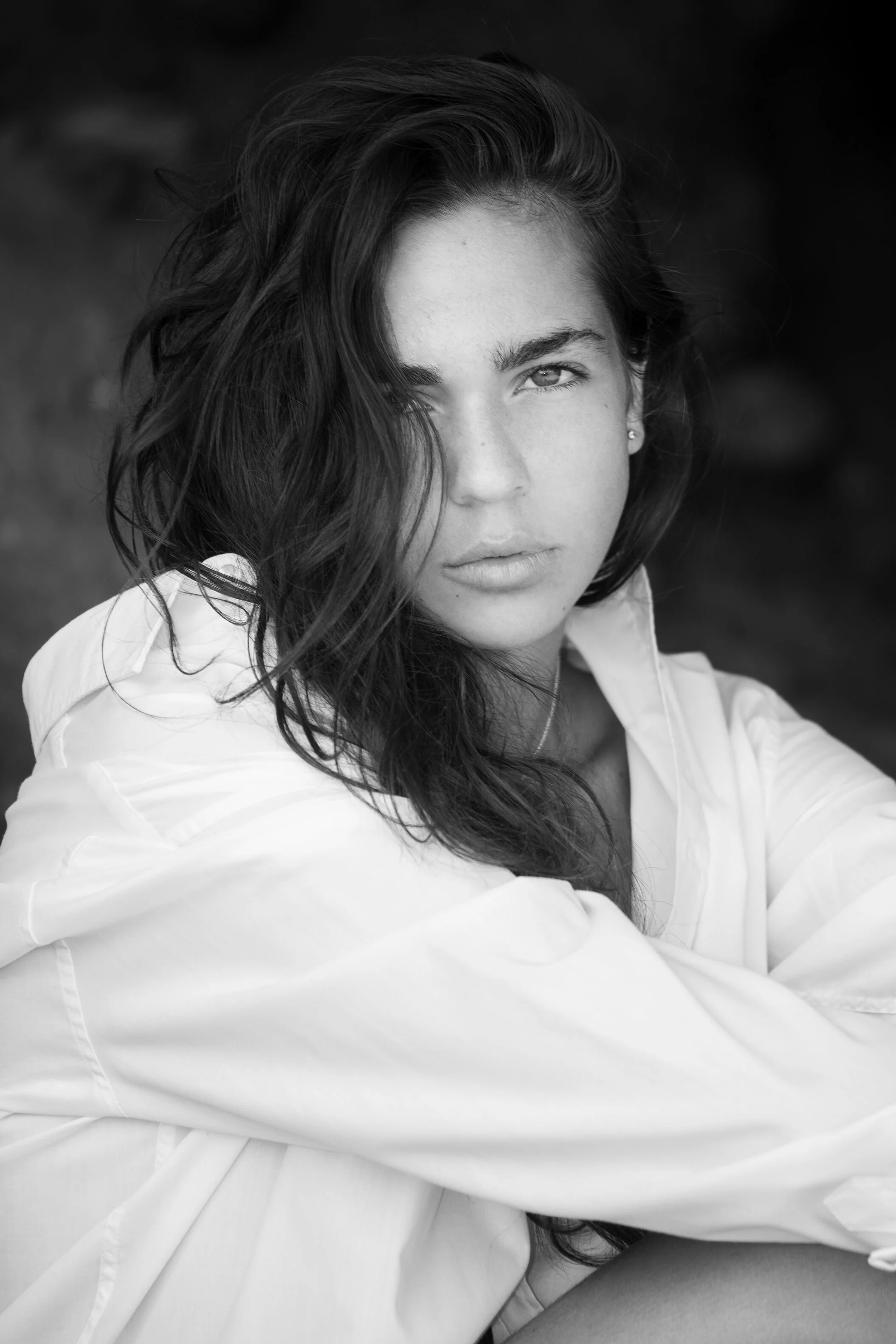 Portrait en noir et blanc d'une jeune femme avec des cheveux ondulés et une expression sérieuse, portant une chemise blanche.