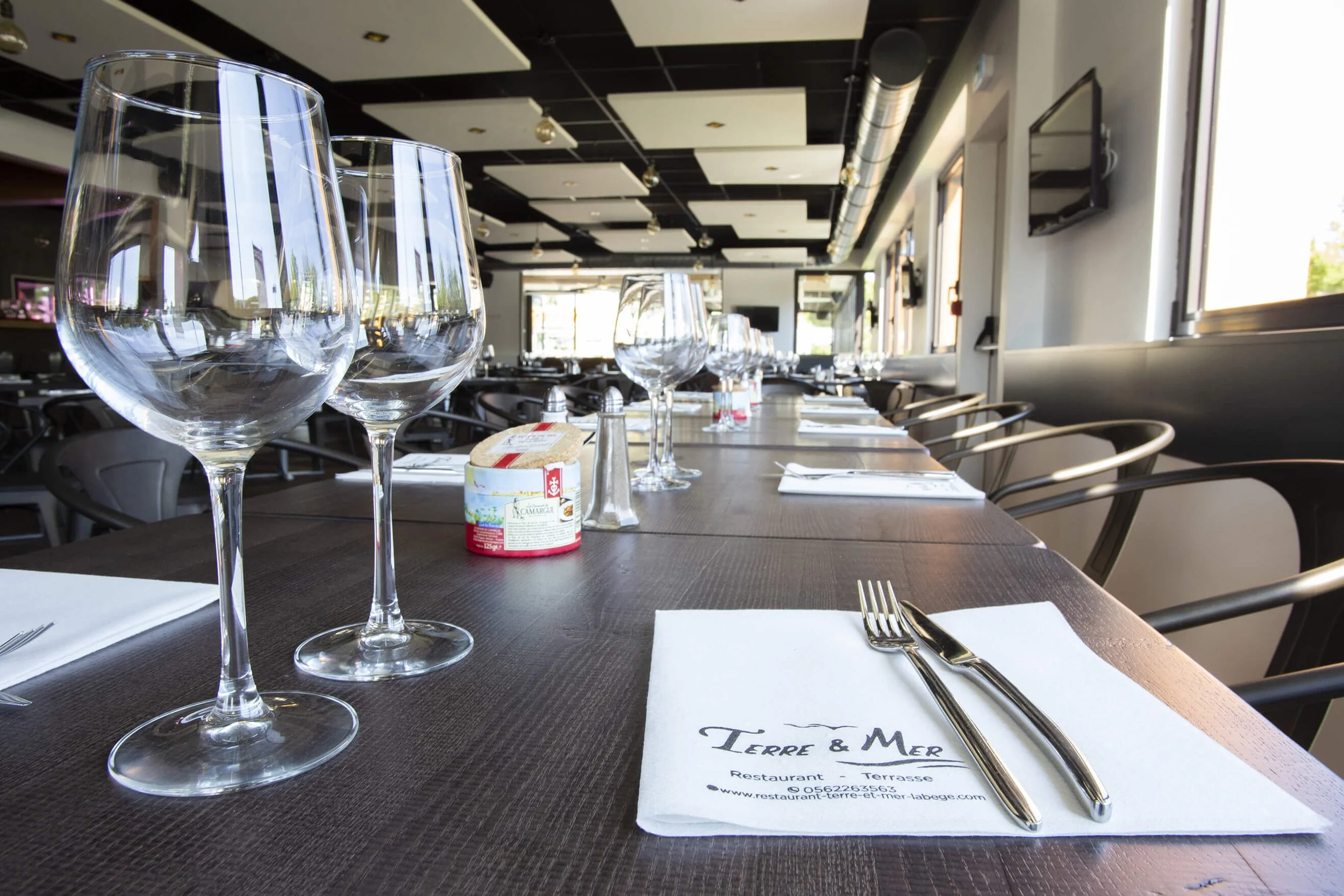 Le restaurant Terre & Mer offre une ambiance élégante et moderne, comme en témoignent ces photographies professionnelles.  Les tables sont soigneusement dressées avec des verres, des couverts et des serviettes impeccablement disposés, créant une atmo