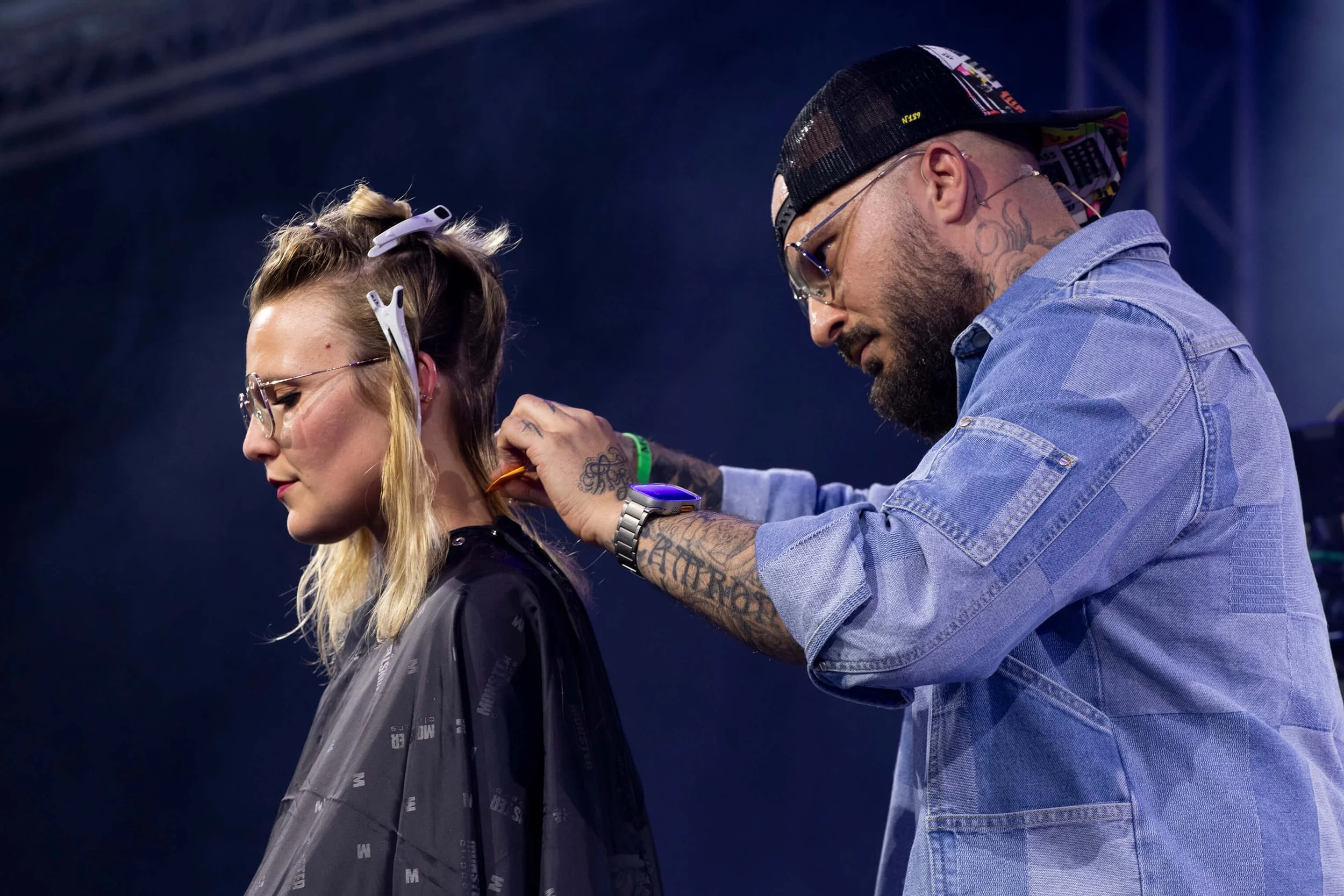 Un coiffeur professionnel en train de créer une coiffure artistique sur une modèle avec des cheveux blonds.