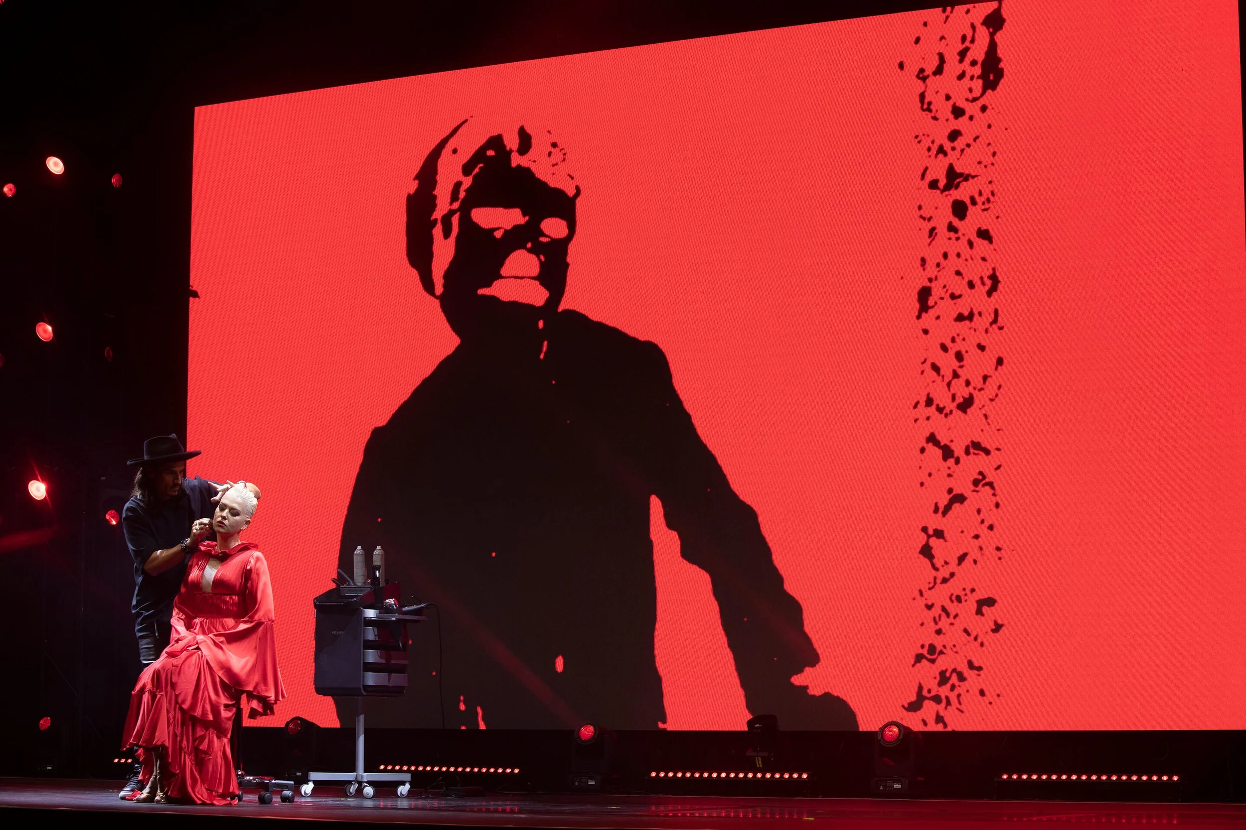 Vue artistique d'une coiffure sur scène avec des couleurs vives
Photographe professionnel capturant l'art de la coiffure en plein spectacle
Coiffure élégante avec un décor rouge et noir en arrière-plan
Mise en scène d'une coiffure avec des lumières e
