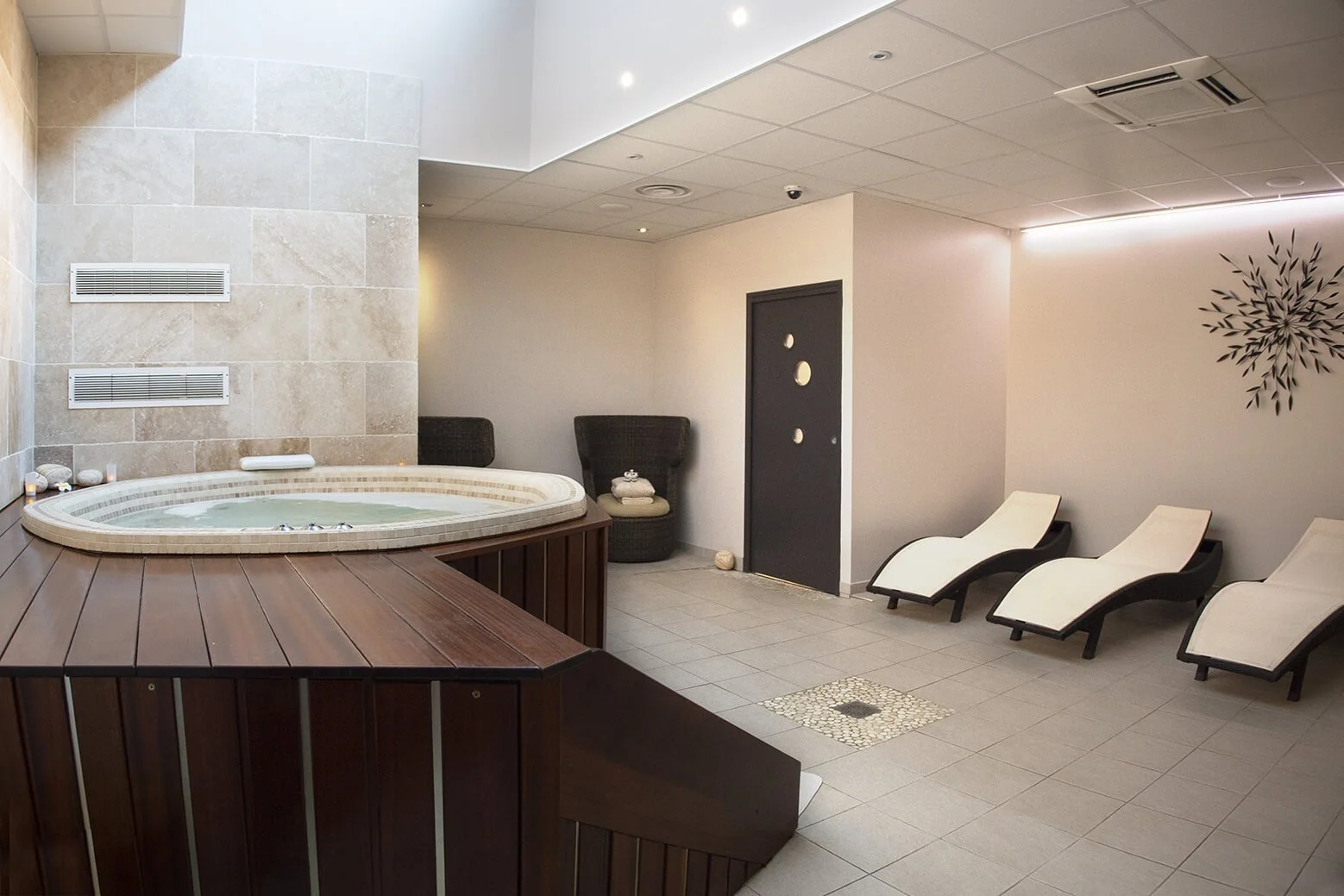 Photographie professionnelle d’un espace de spa moderne, capturant le style et le décor élégant. Le jacuzzi, entouré de chaises longues, invite à la détente.  L’ambiance relaxante est sublimée par les couleurs douces et le décor raffiné, mettant en v