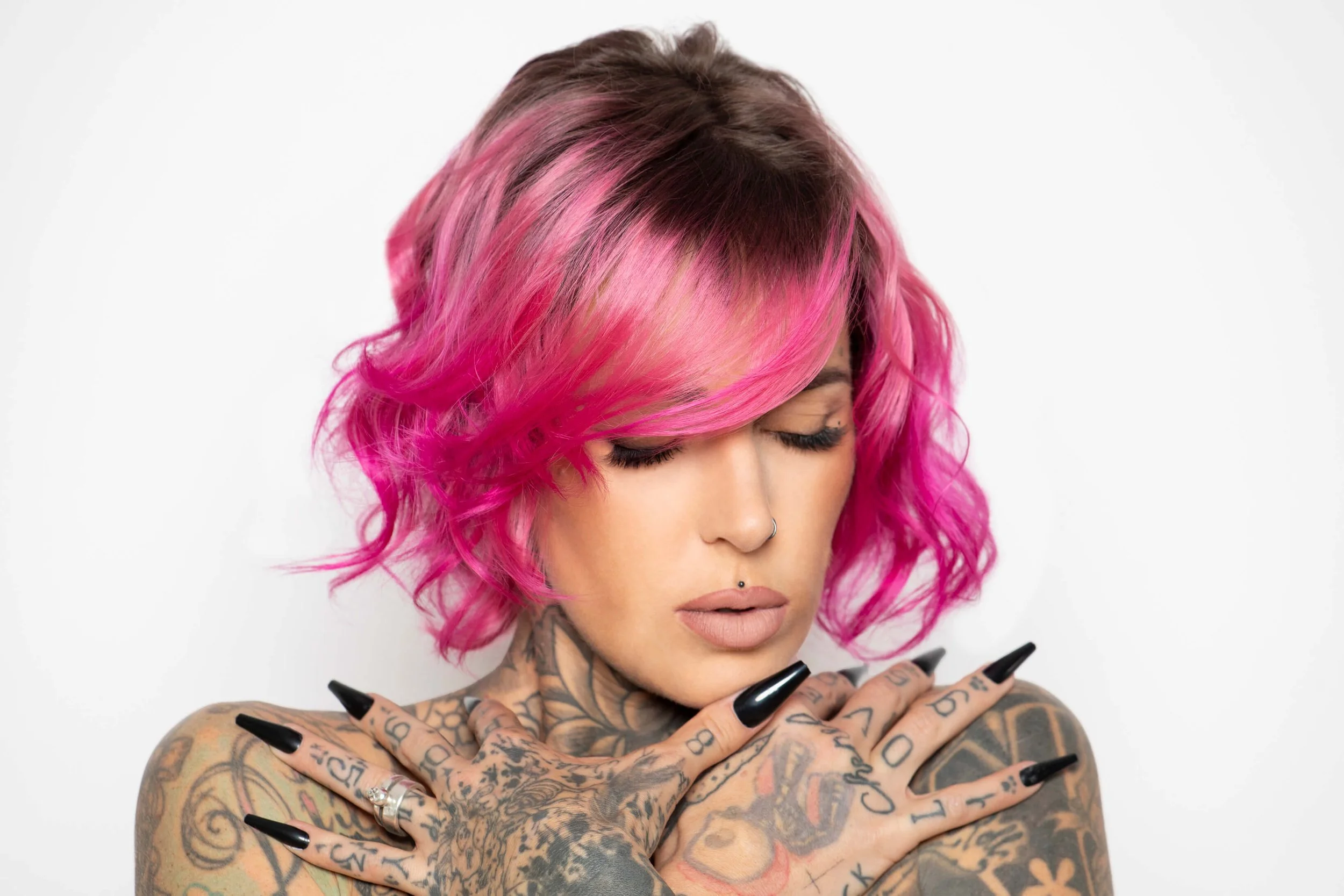 Portrait d'une femme avec des cheveux bouclés roses et des ongles noirs, mettant en valeur l'art de la coiffure.